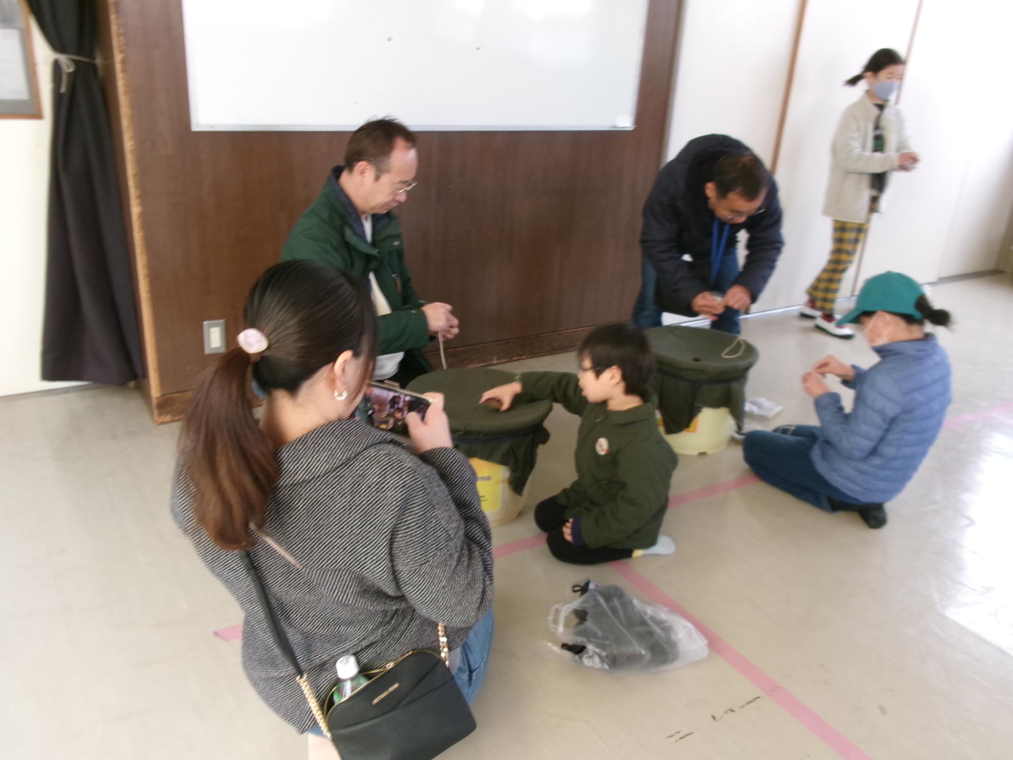 昔遊び体験ブースでベイゴマを地域の方と一緒に遊ぶ子どもたちの写真