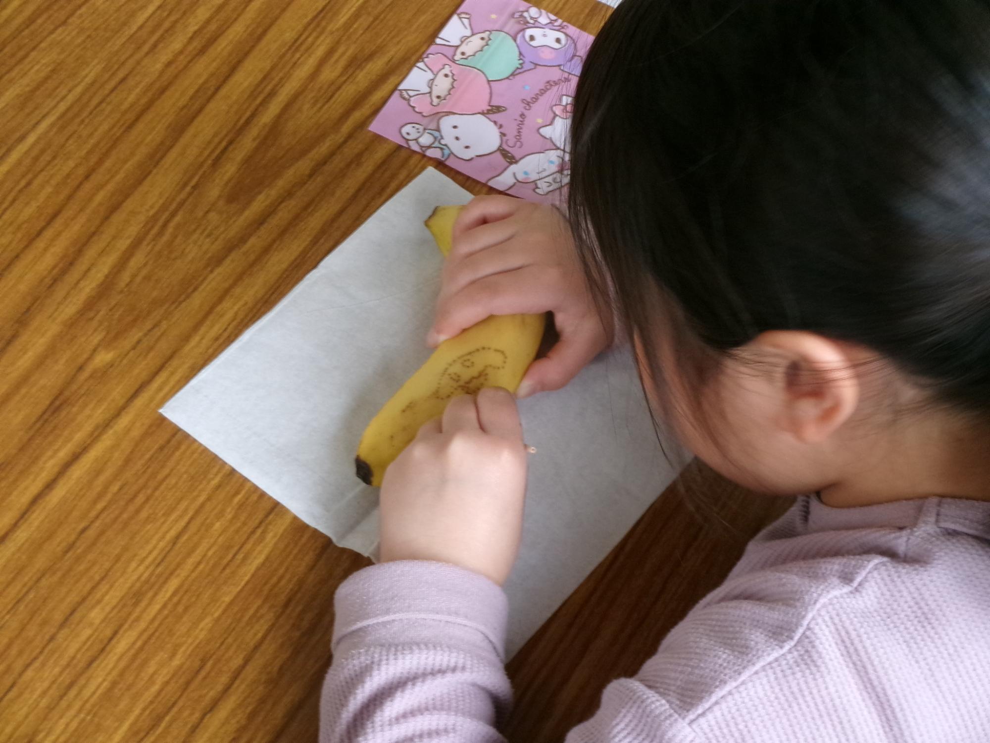 児童がつまようじでバナナの皮に穴をあけて絵を描いている様子の写真