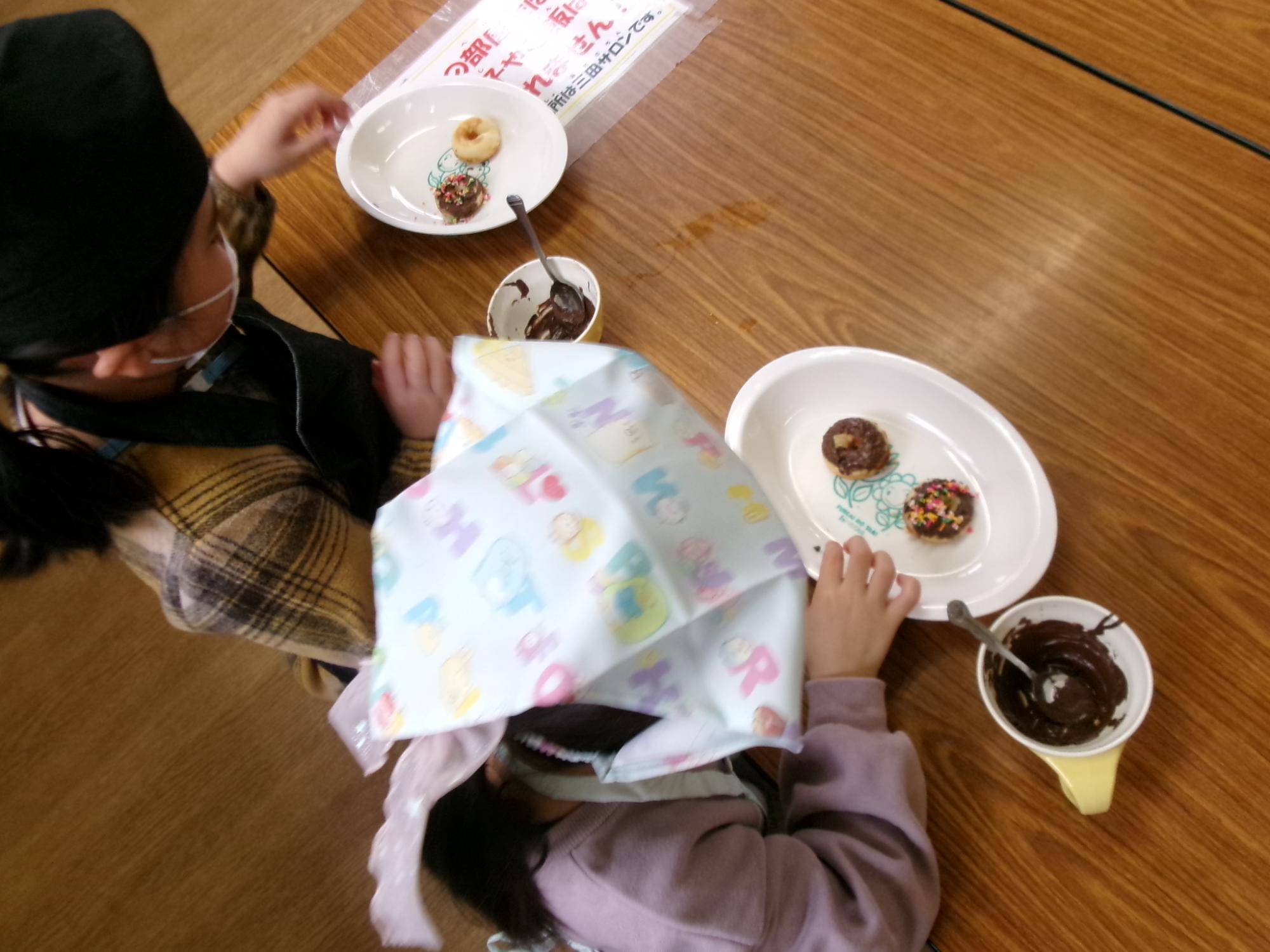 児童がドーナツにチョコをかけている様子の写真