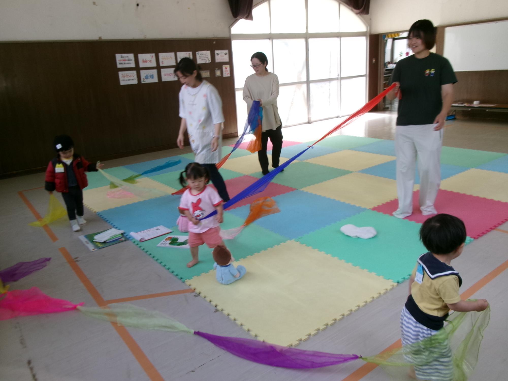 乳幼児親子がカラフルなガーゼをつないで遊んでいる様子