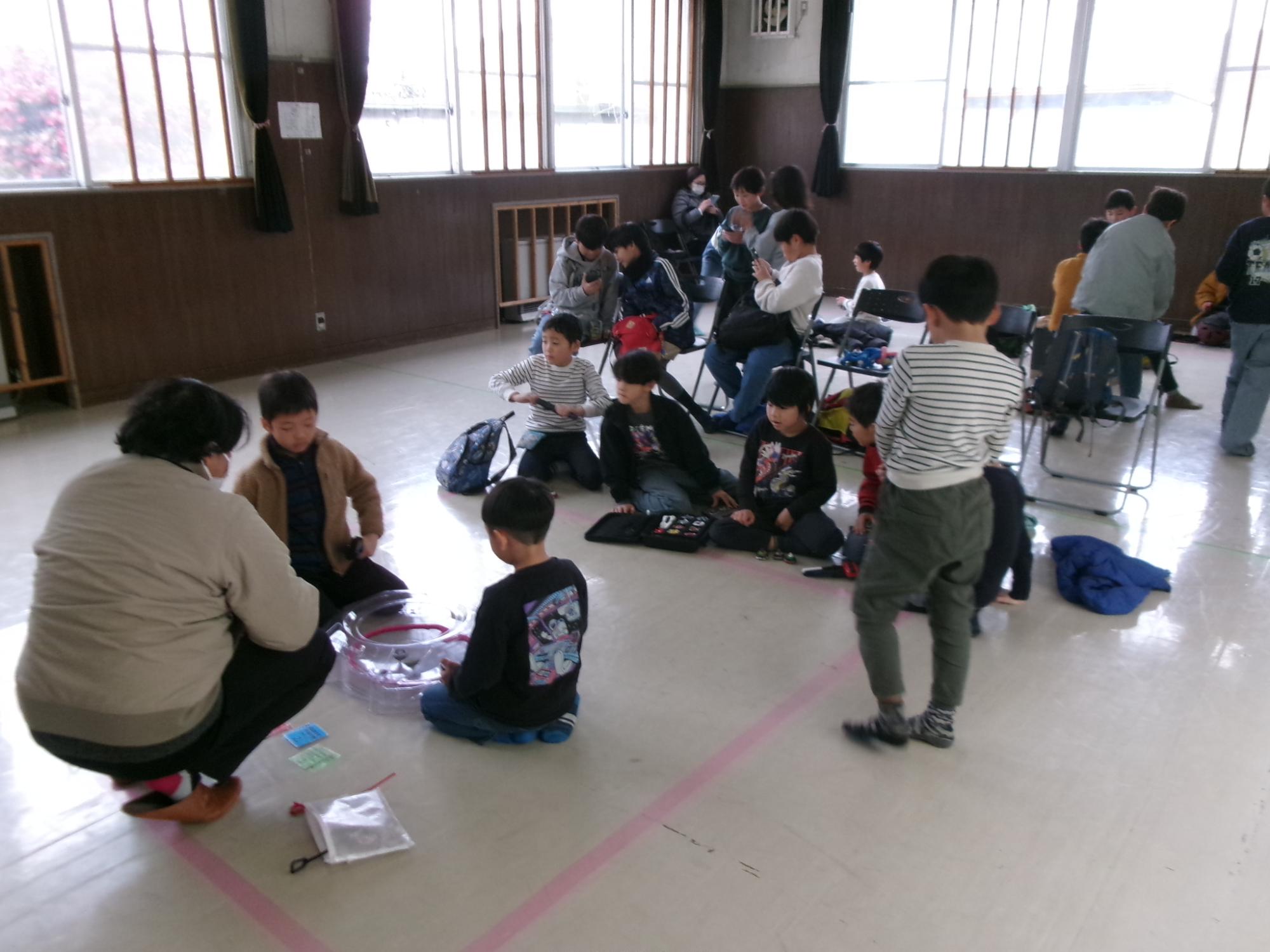 ベイブレードの試合をしている子どもたちと、それを観戦している子どもたちの写真