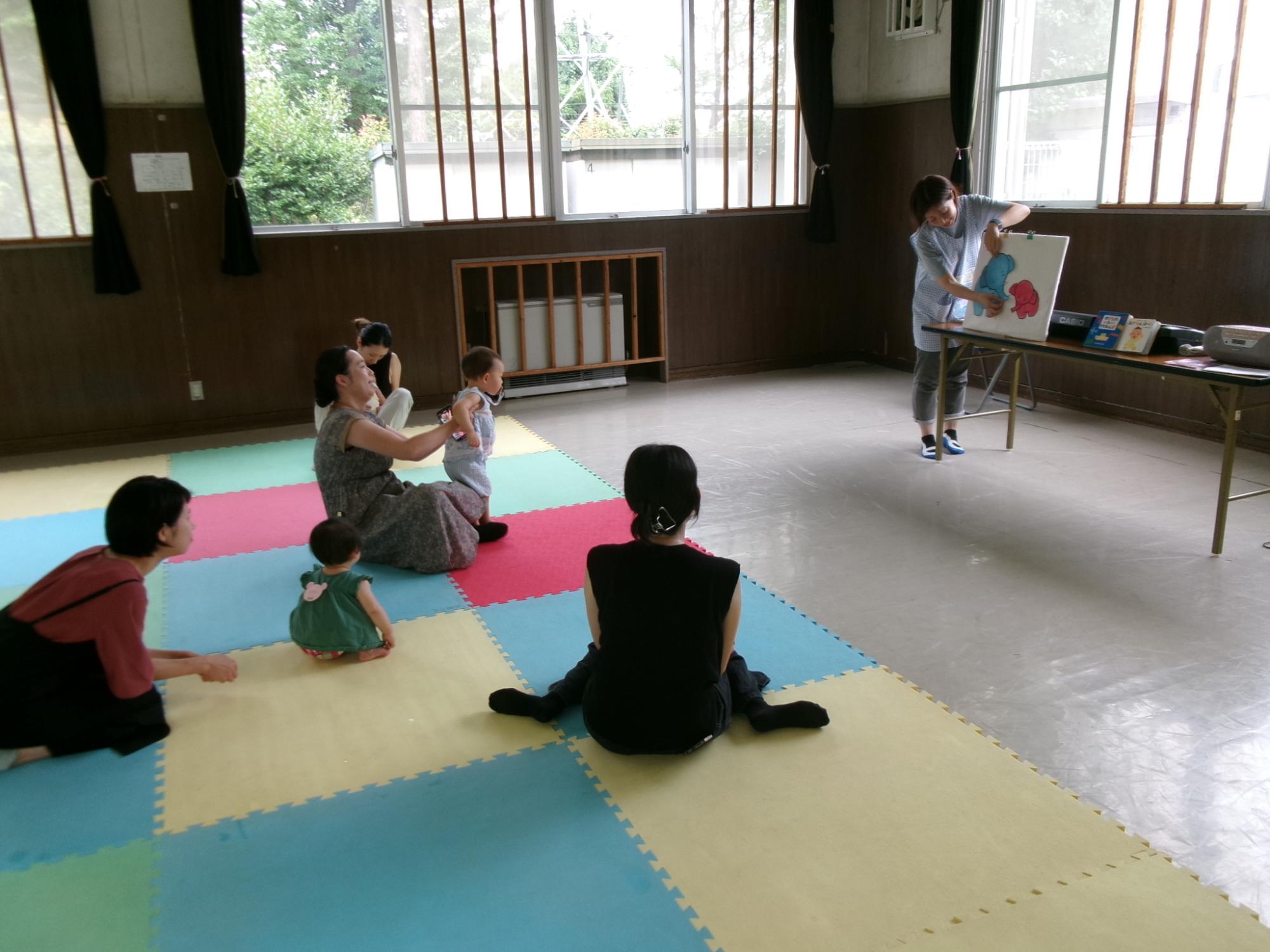 講師が読んでいる紙芝居を聞いている幼児親子の様子の写真