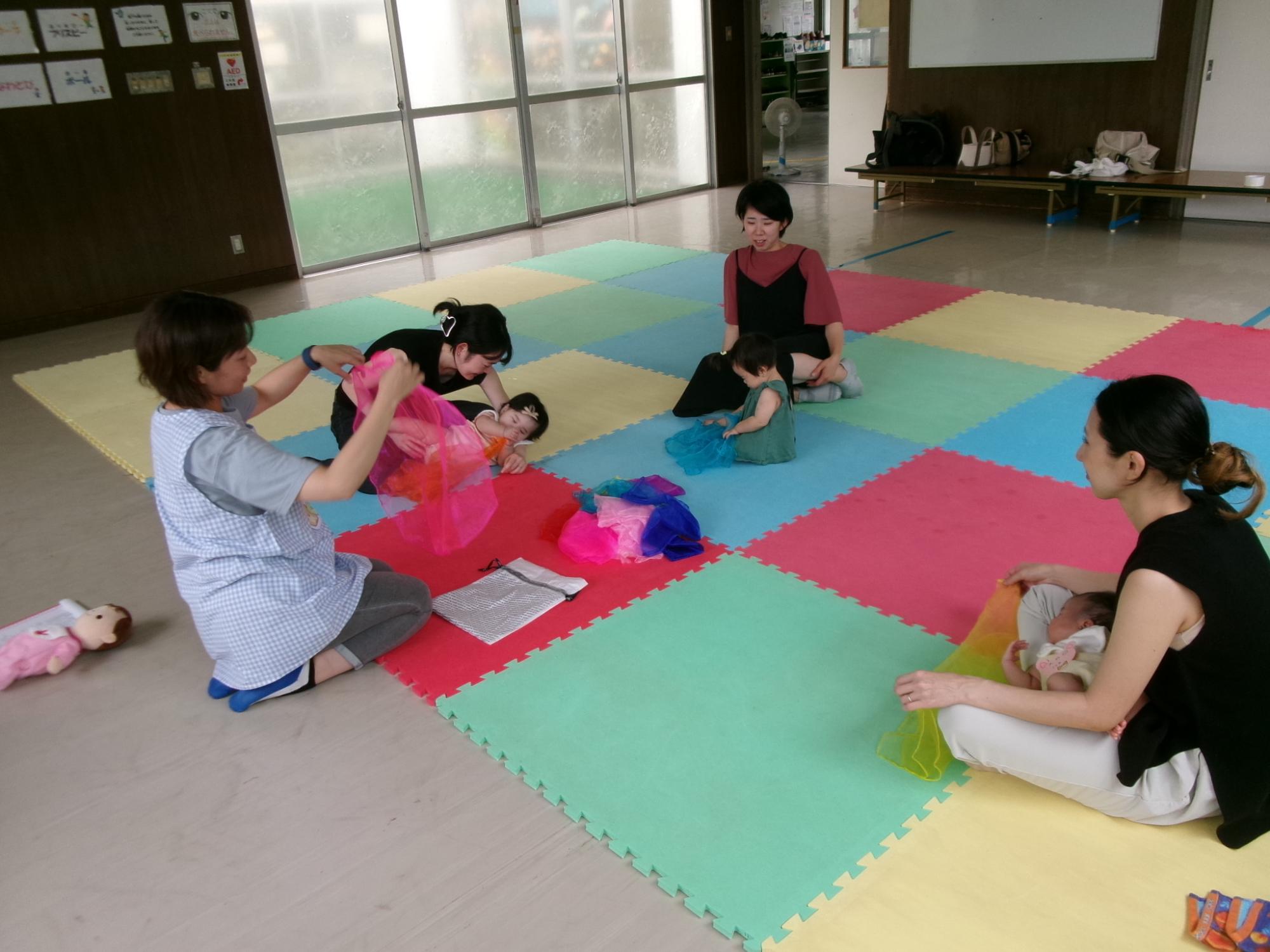 幼児親子が、薄い布やフェルト生地の感触を顔や体で楽しむ遊びをしている様子の写真