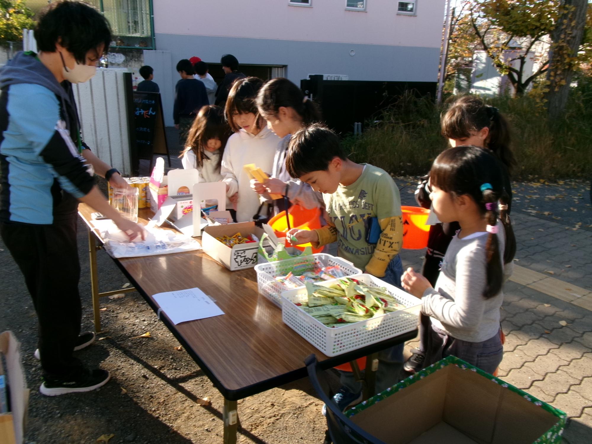 園庭で駄菓子を販売し小学生が選んで購入している様子の写真
