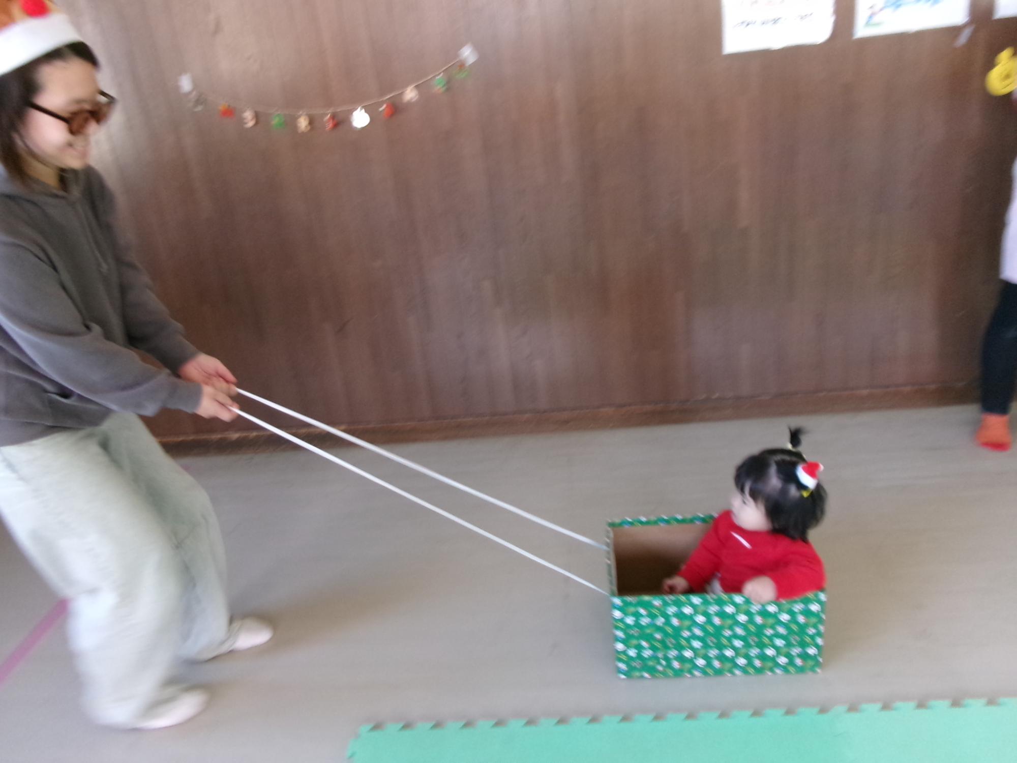 箱のそりに乗って引っ張られている幼児の写真