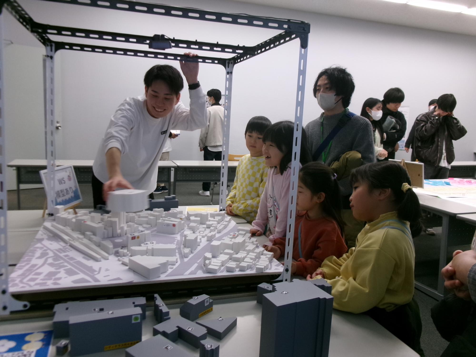 建物の模型を動かして、建物による人の流れを予測する研究を見学する子どもたちの様子の写真