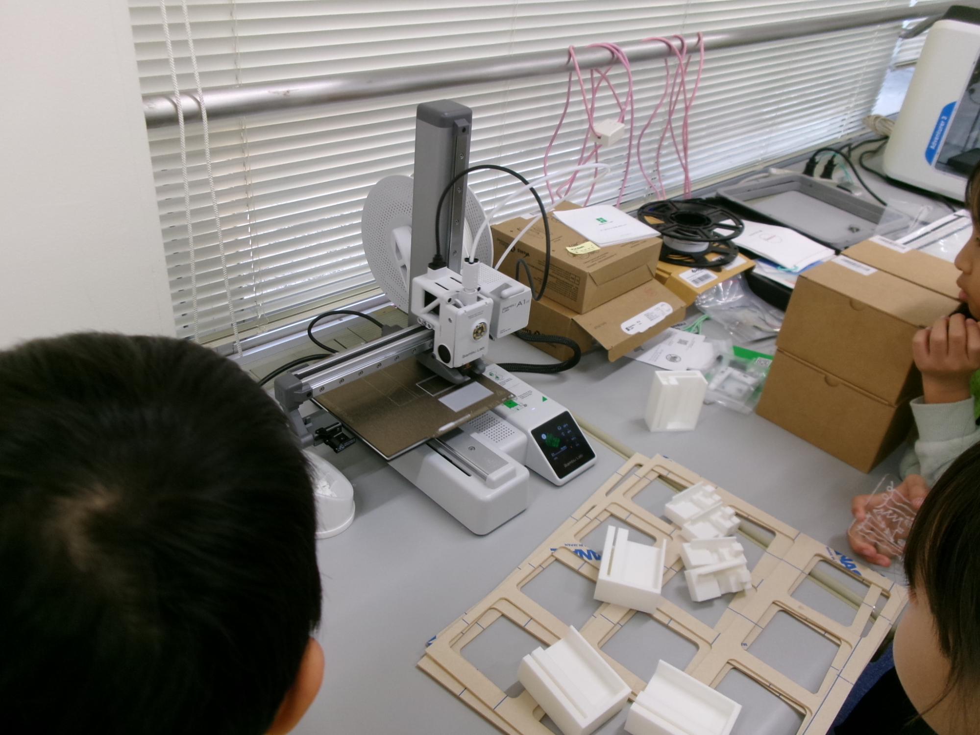 稼働している3Dプリンターを見学している子どもたちの写真