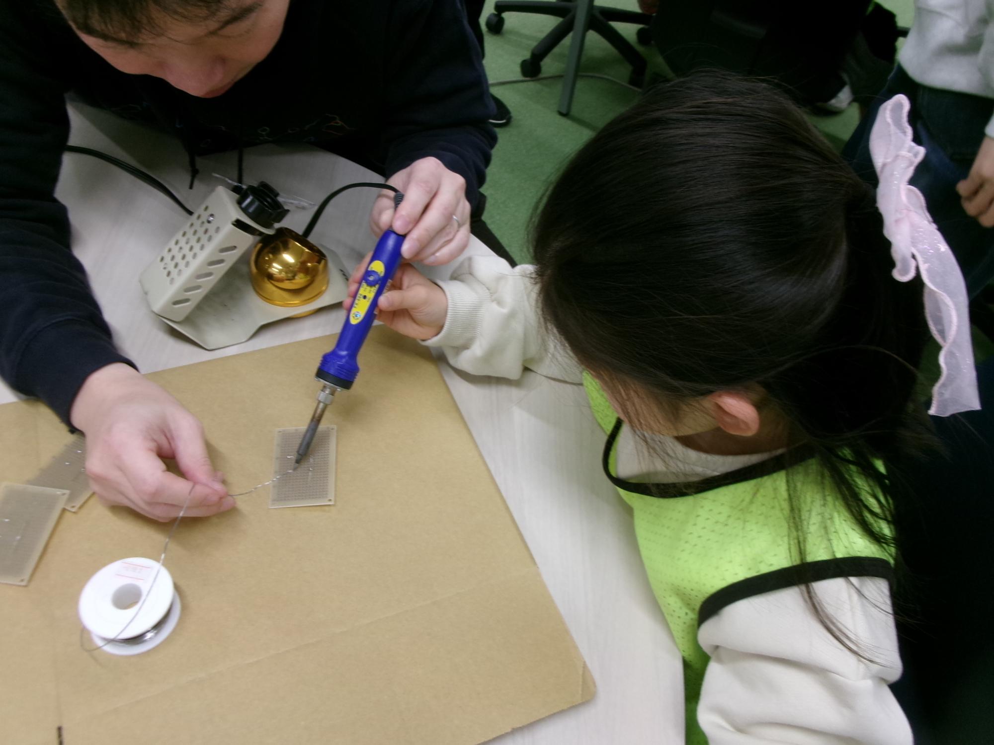 専修大学の先生と一緒にはんだごての使用体験をしている子どもの写真