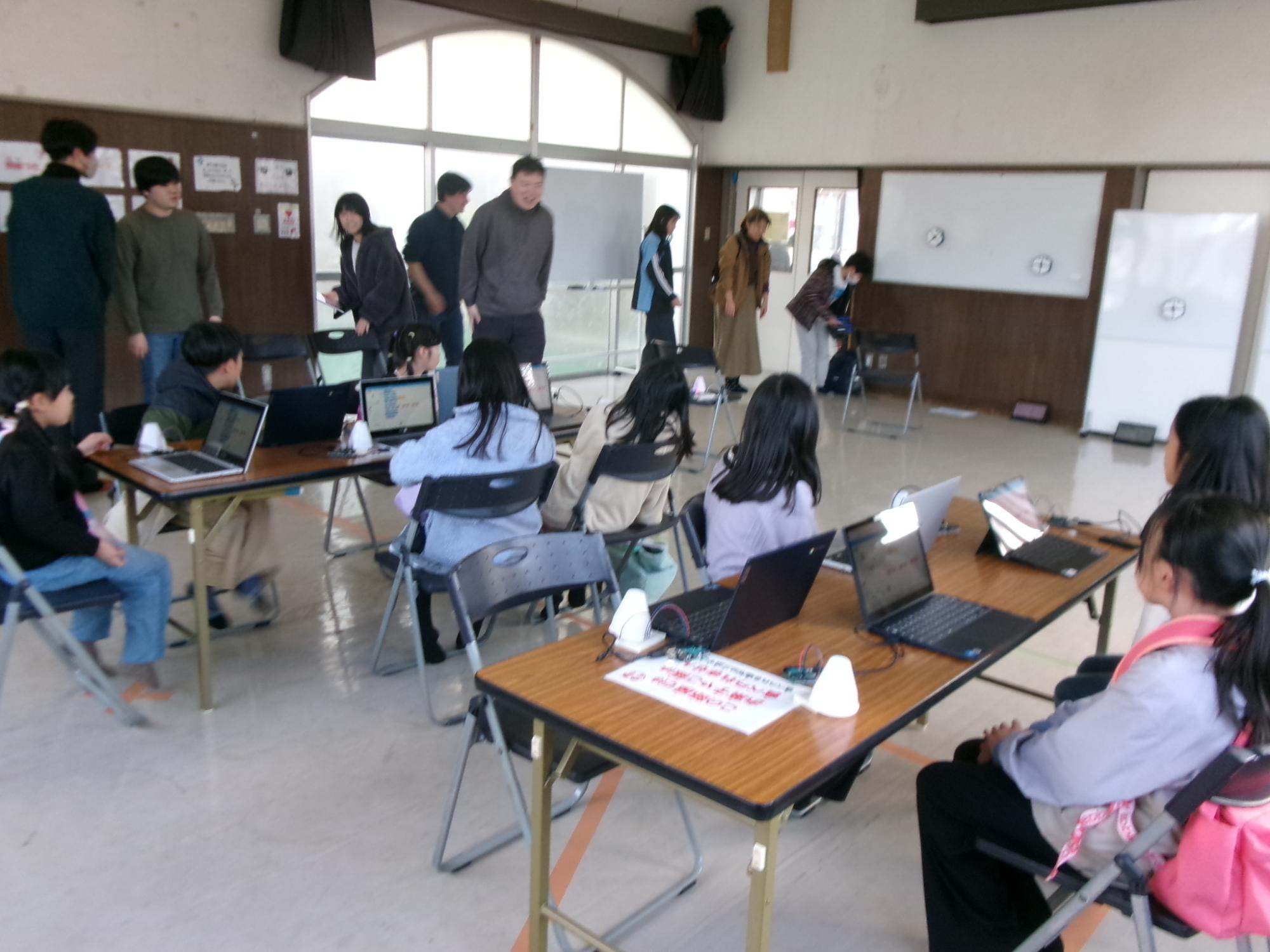 タブレットが置かれた机の前で座って説明を受けている参加者の写真