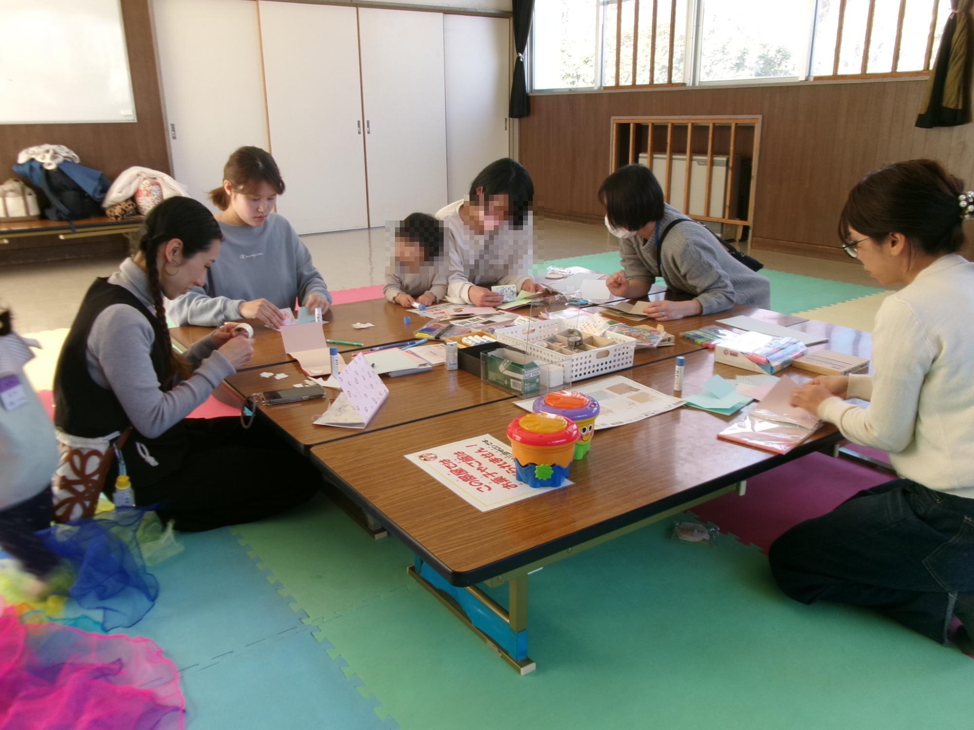 テーブルを囲んで乳幼児親子がアルバム工作をしている様子