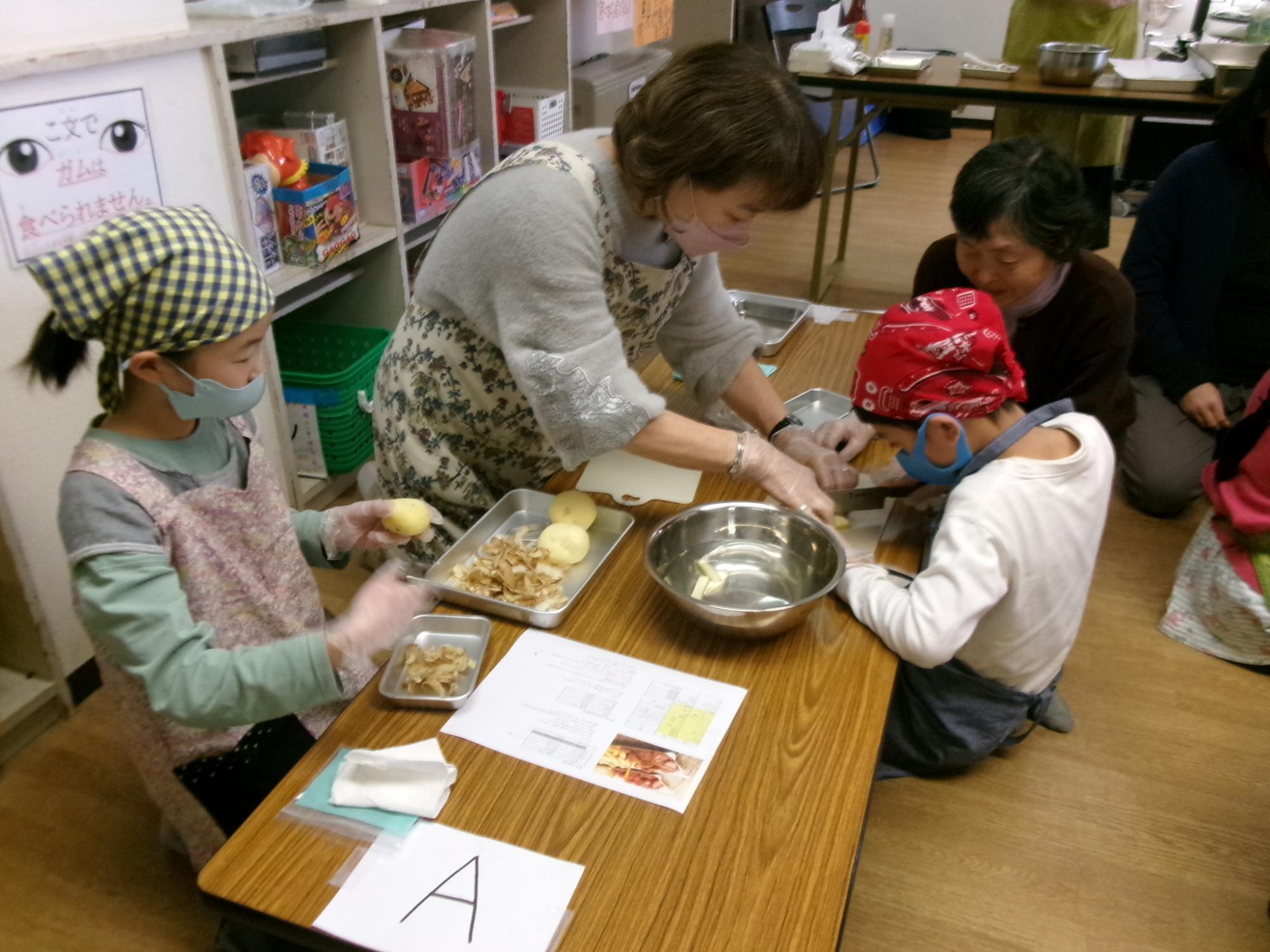 児童と地域住民がドイツ料理の調理でジャガイモの皮をむいている様子