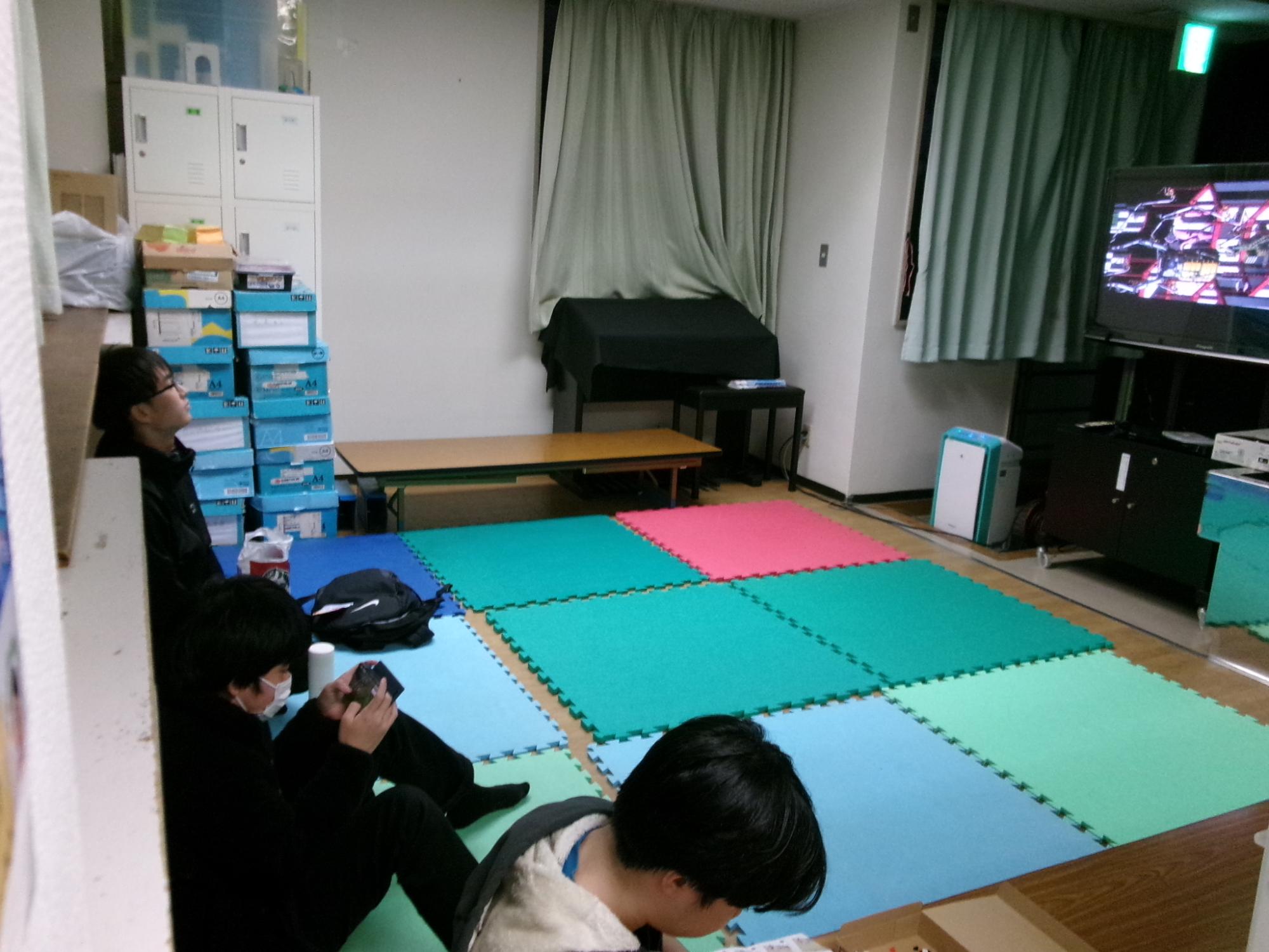 マットの上に座って映画を見る中学生の写真