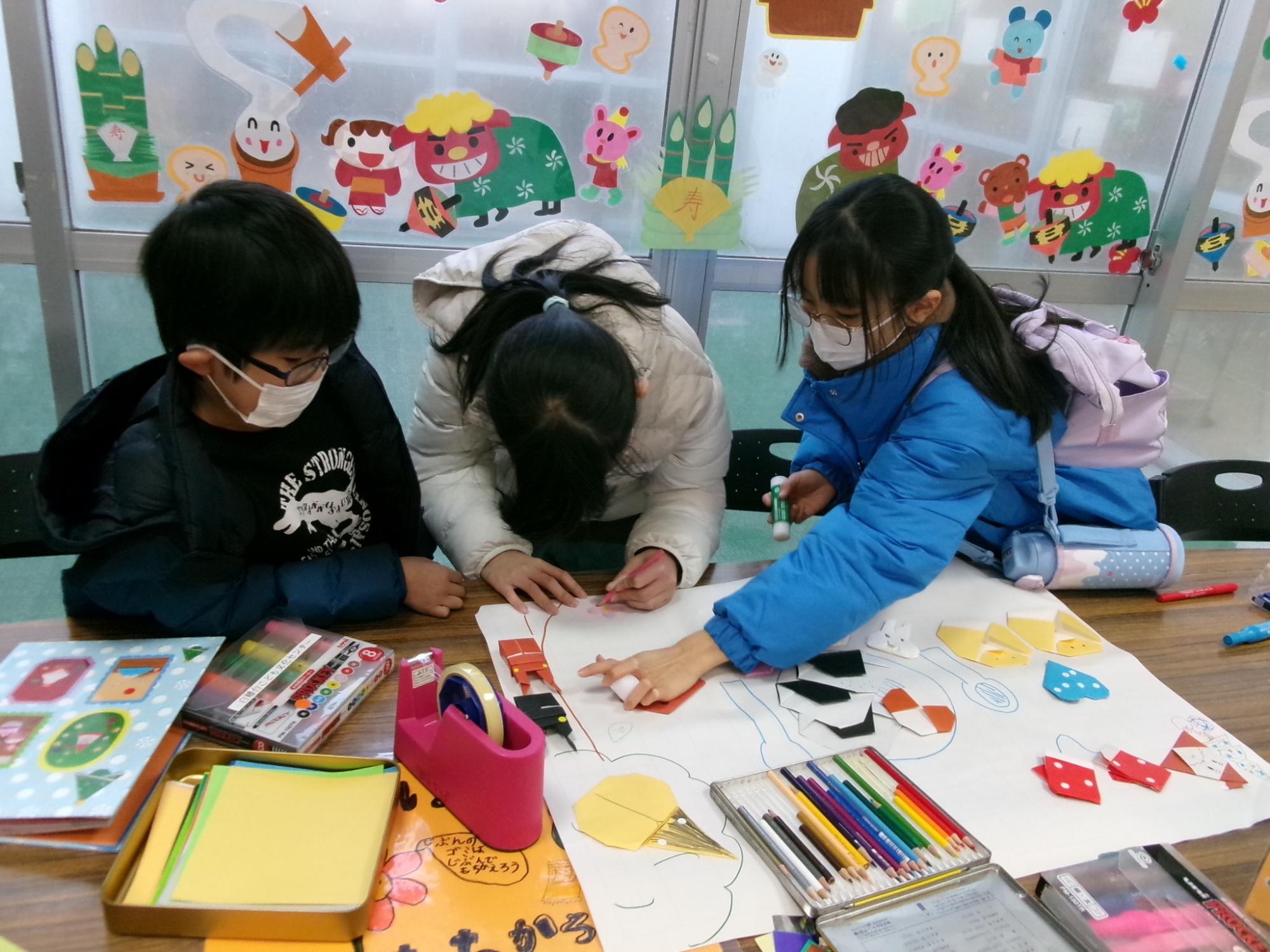3人の小学生が模造紙に作品をはっている写真