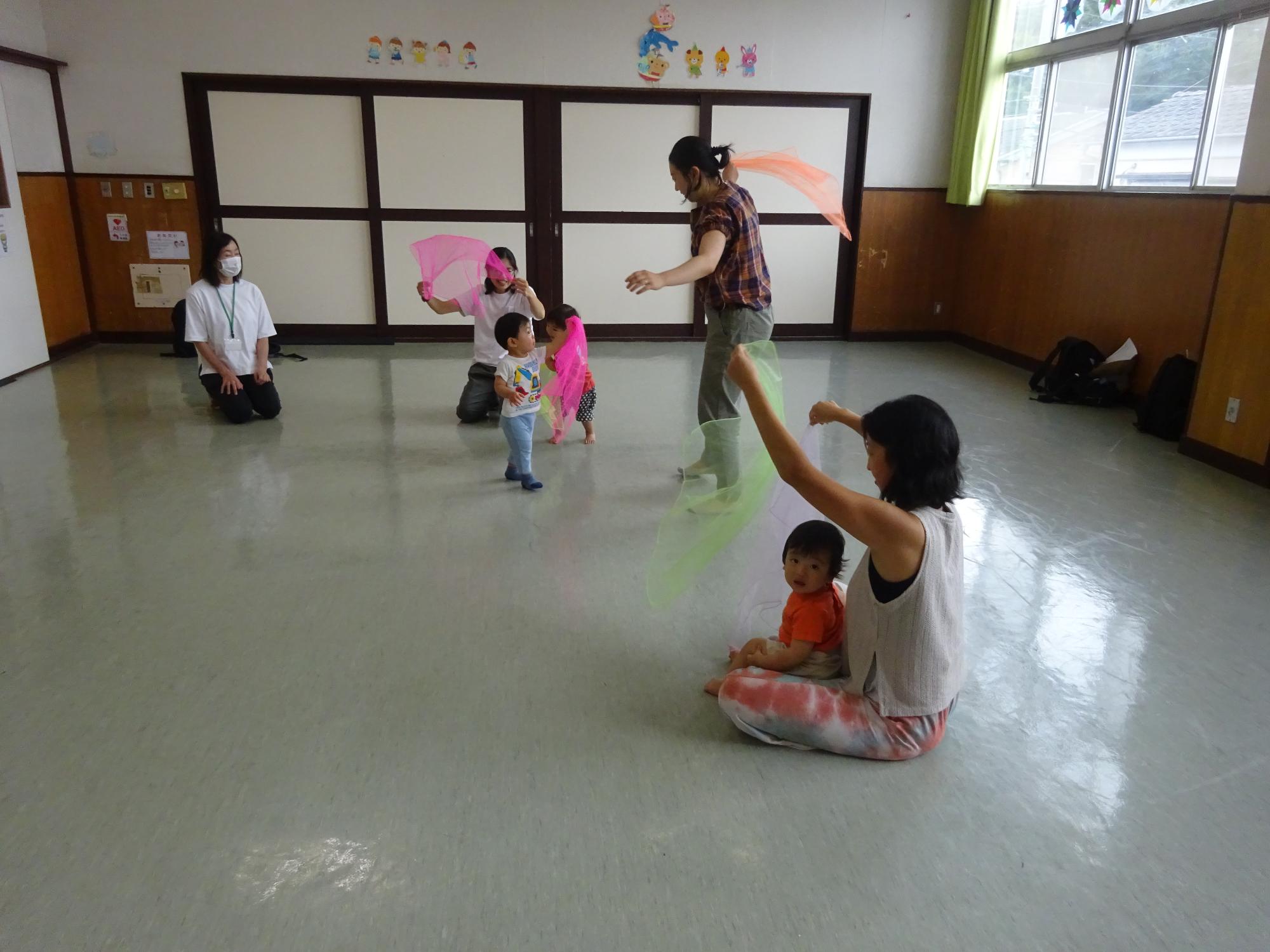 音楽に合わせてシフォン布で遊んでいる幼児親子の写真