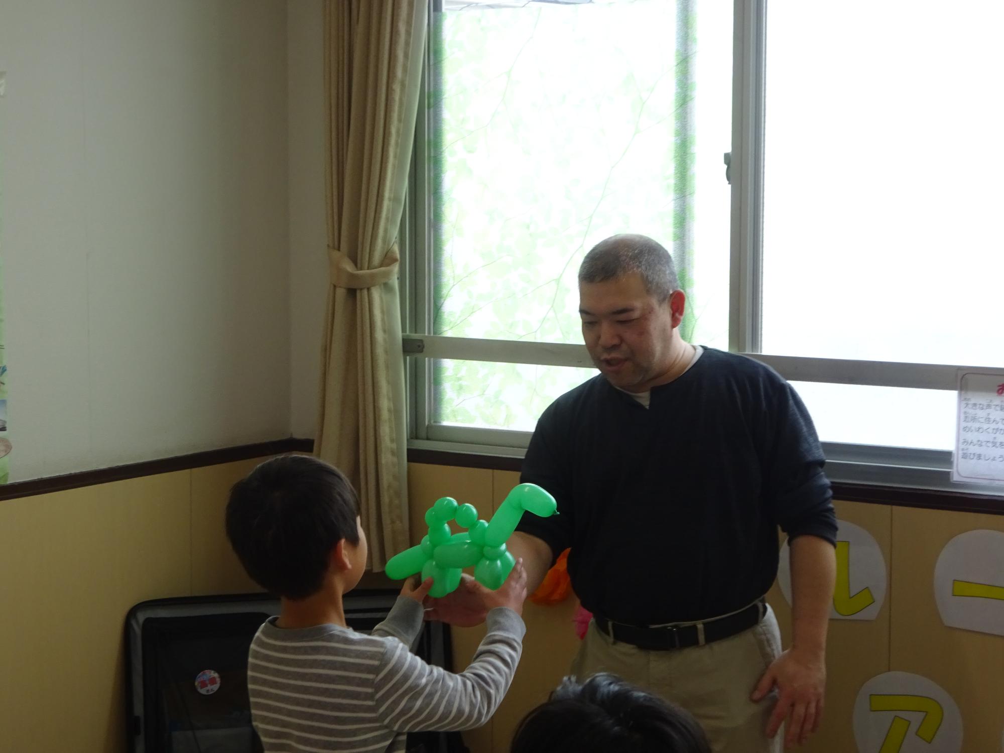 恐竜のバルーンアートをプレゼントしてもらっている子どもの写真