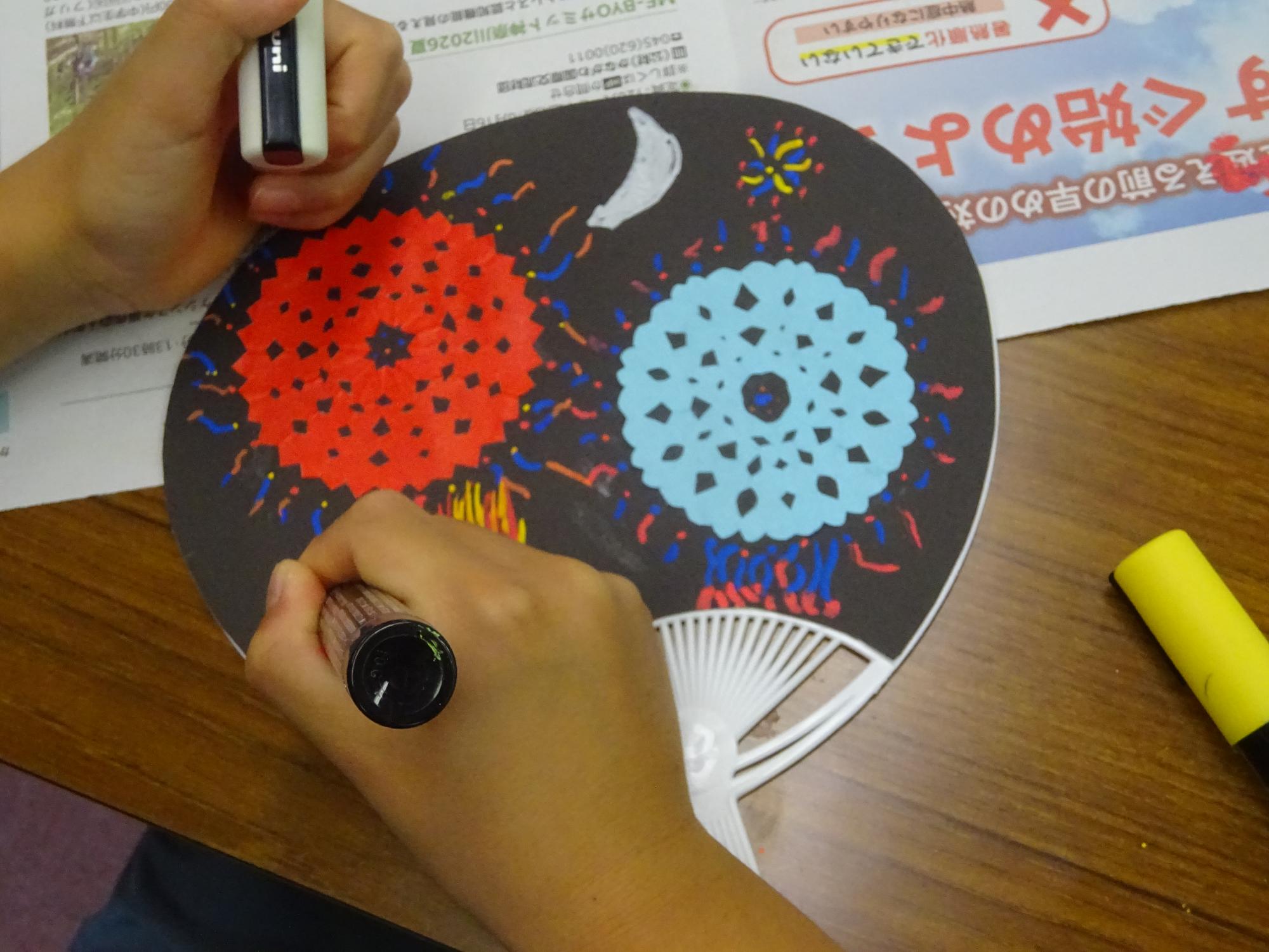 うちわに花火を描いている子どもの写真