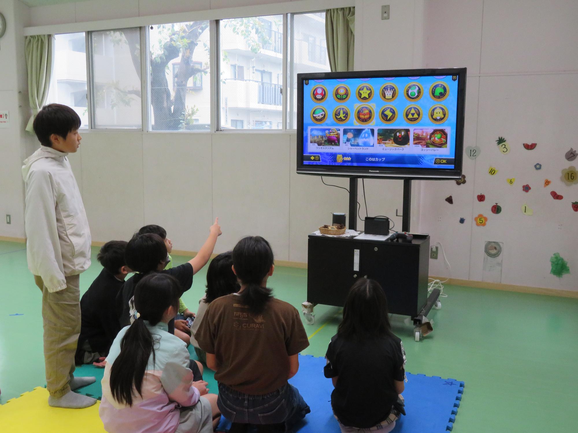 緑の床に敷いてあるマットに座ってゲームをしている子どもたちの写真