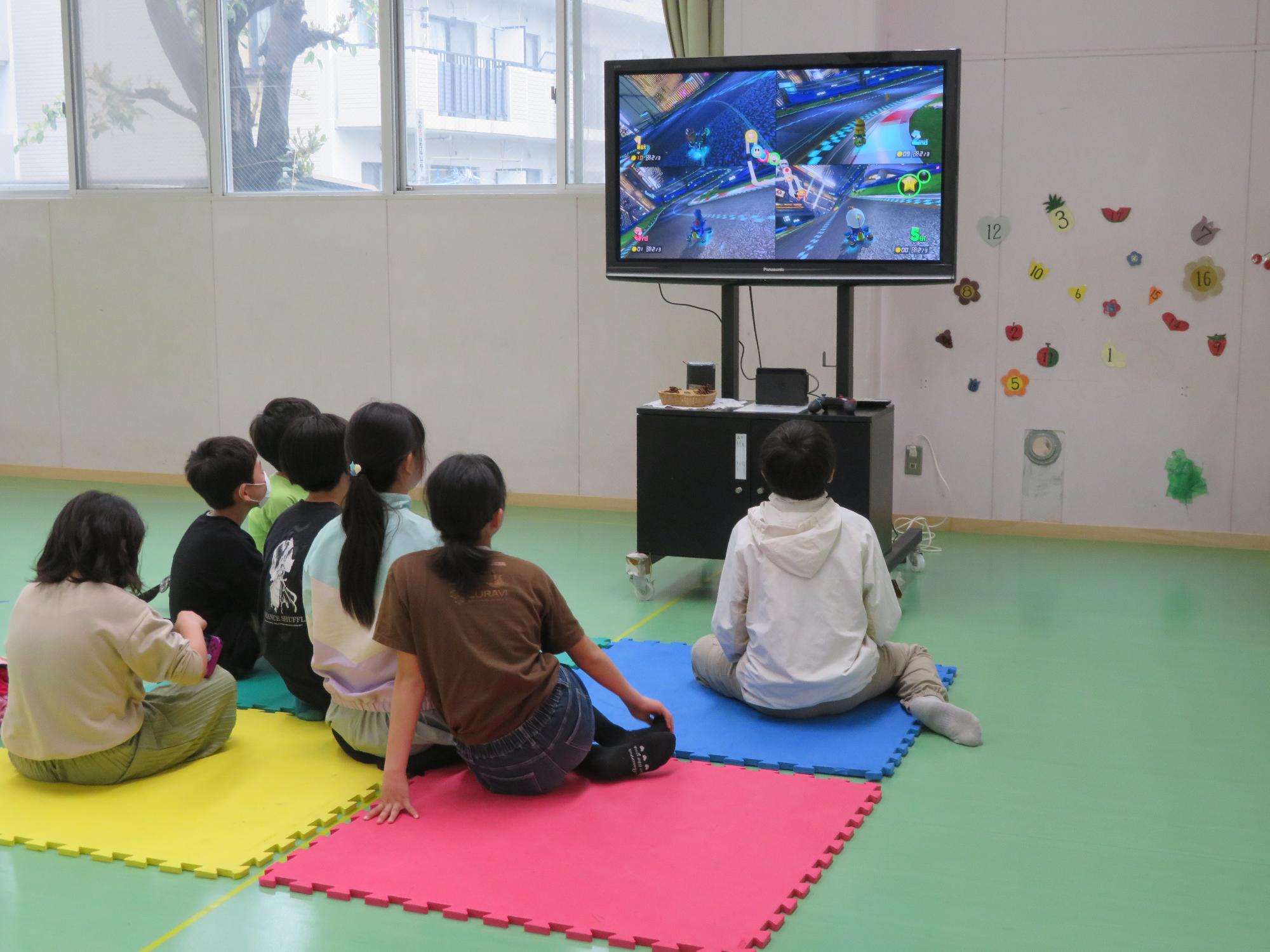 緑色の床に敷いてあるマットに座って子どもたちがゲームをしている写真