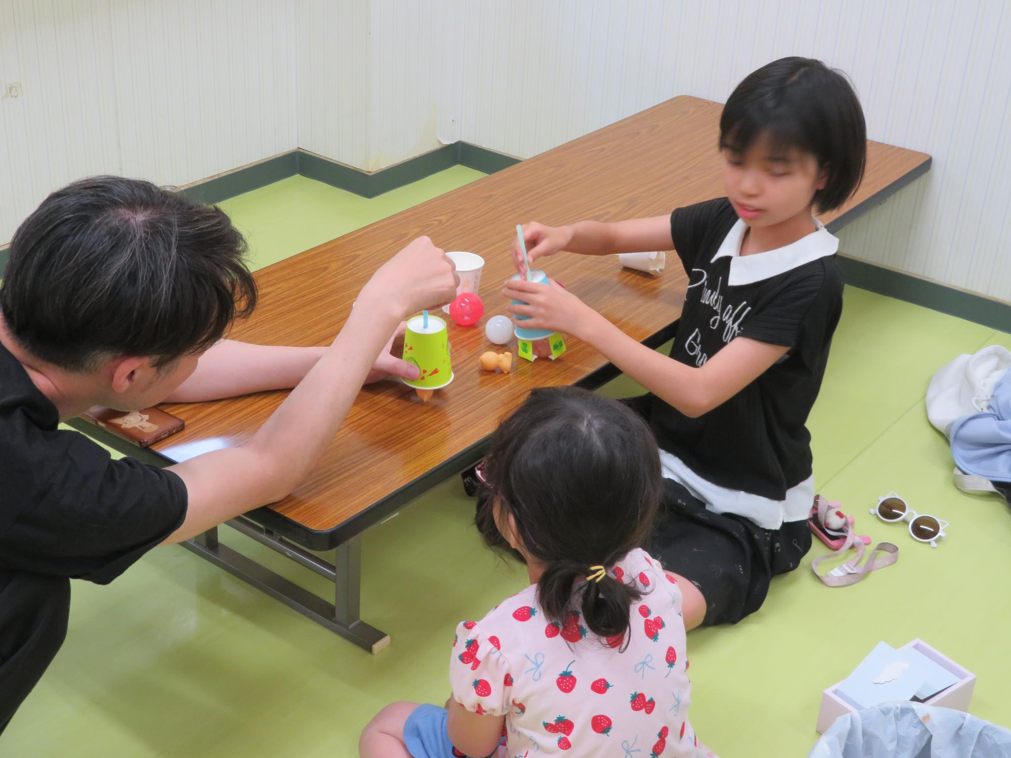 幼児さんに作った工作の遊び方を教えている小学生児童の写真