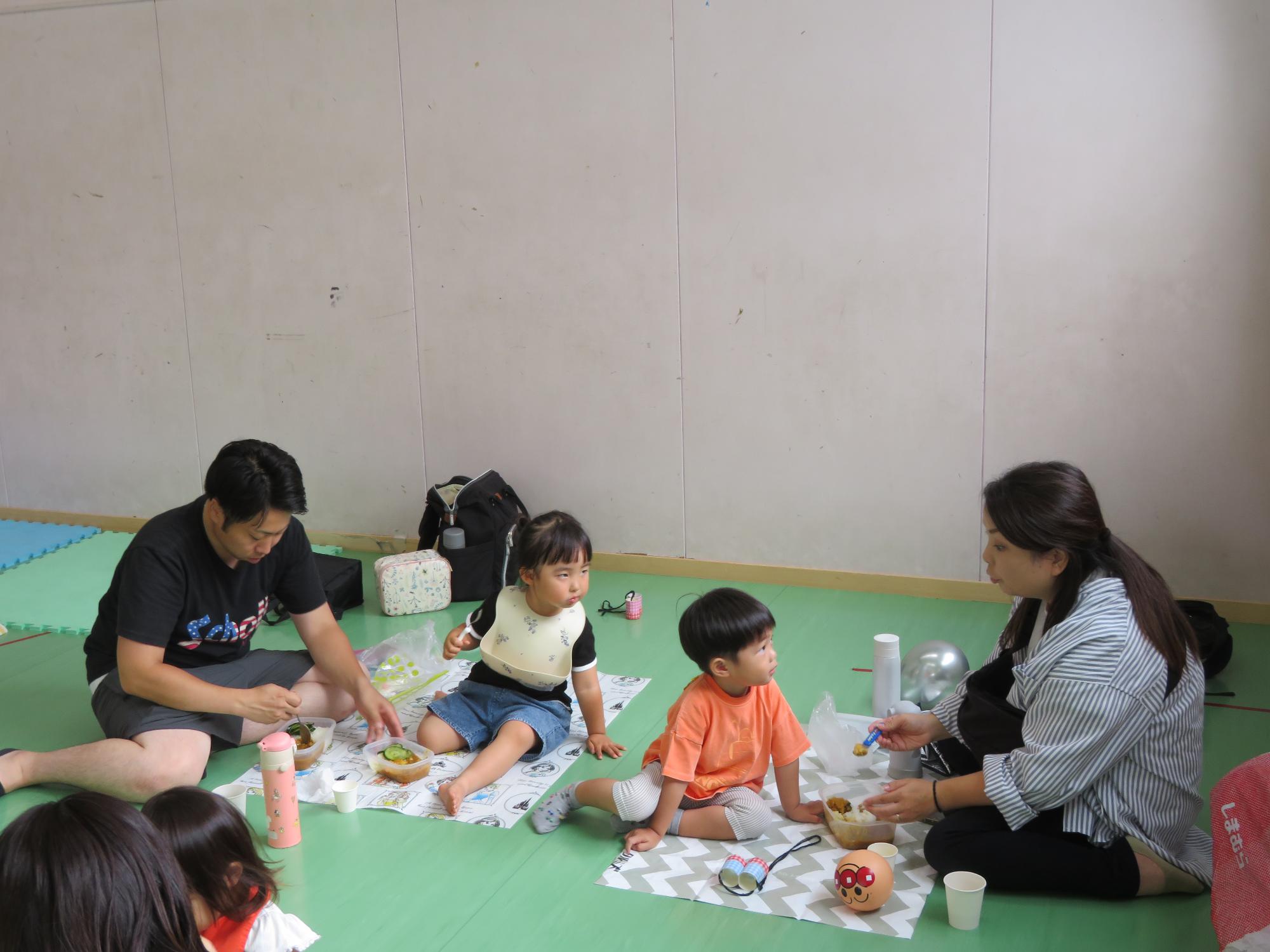 レジャーシートを広げてカレーを食べる乳幼児親子の様子の写真