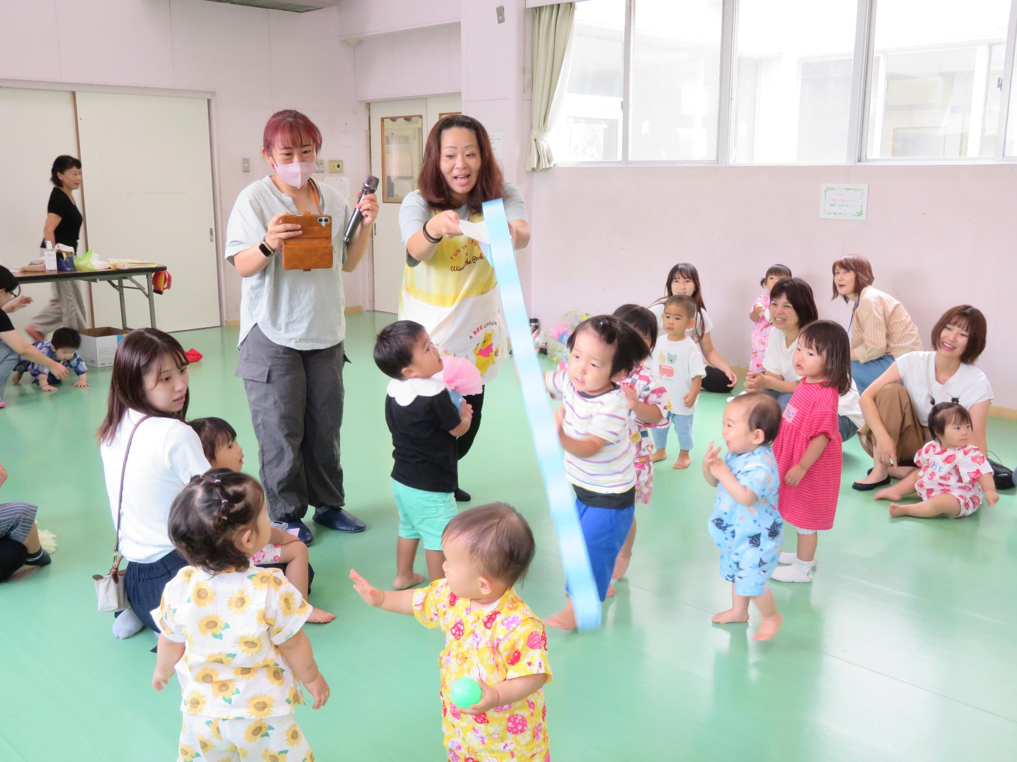幼児サークルの先生による手遊びに夢中になる乳幼児の様子の写真