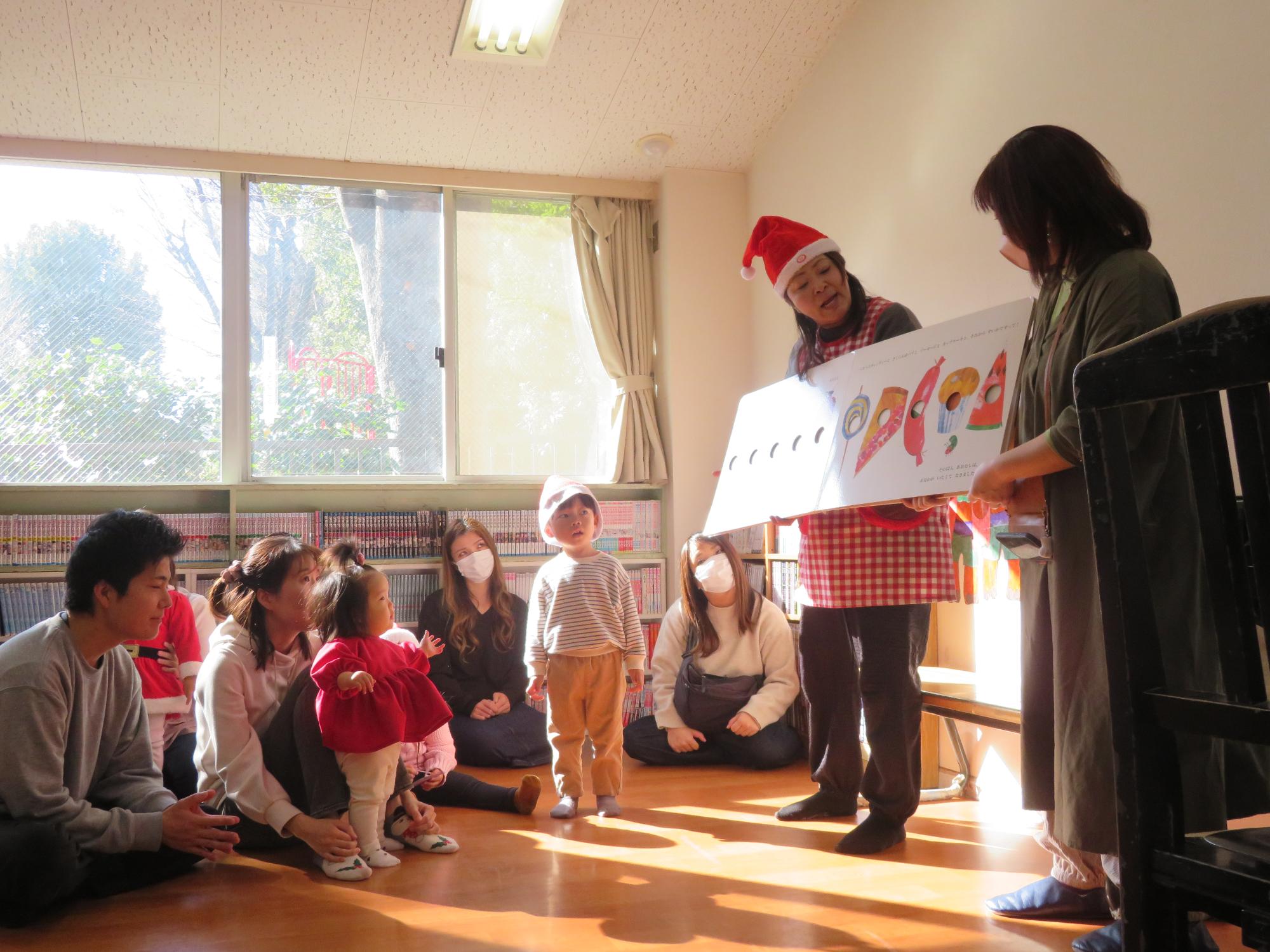 読み聞かせをする先生と真剣な様子で絵本を見つめる幼児親子の様子の写真