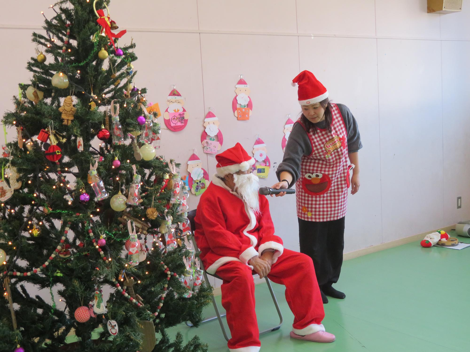 サンタに扮した地域ボランティアの方にインタビューをする先生の写真