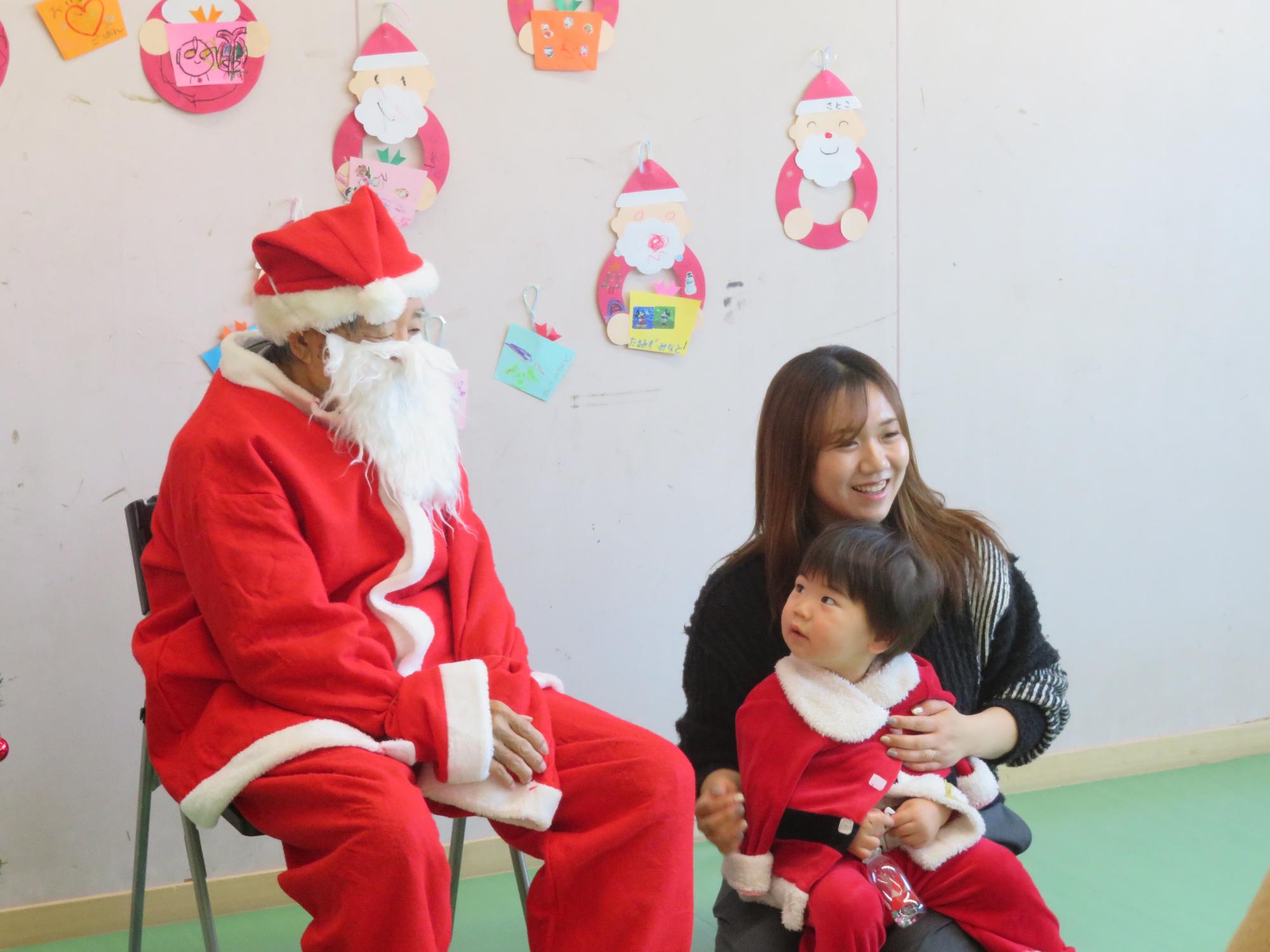 サンタに扮した地域ボランティアの方と写真を撮る幼児親子の写真