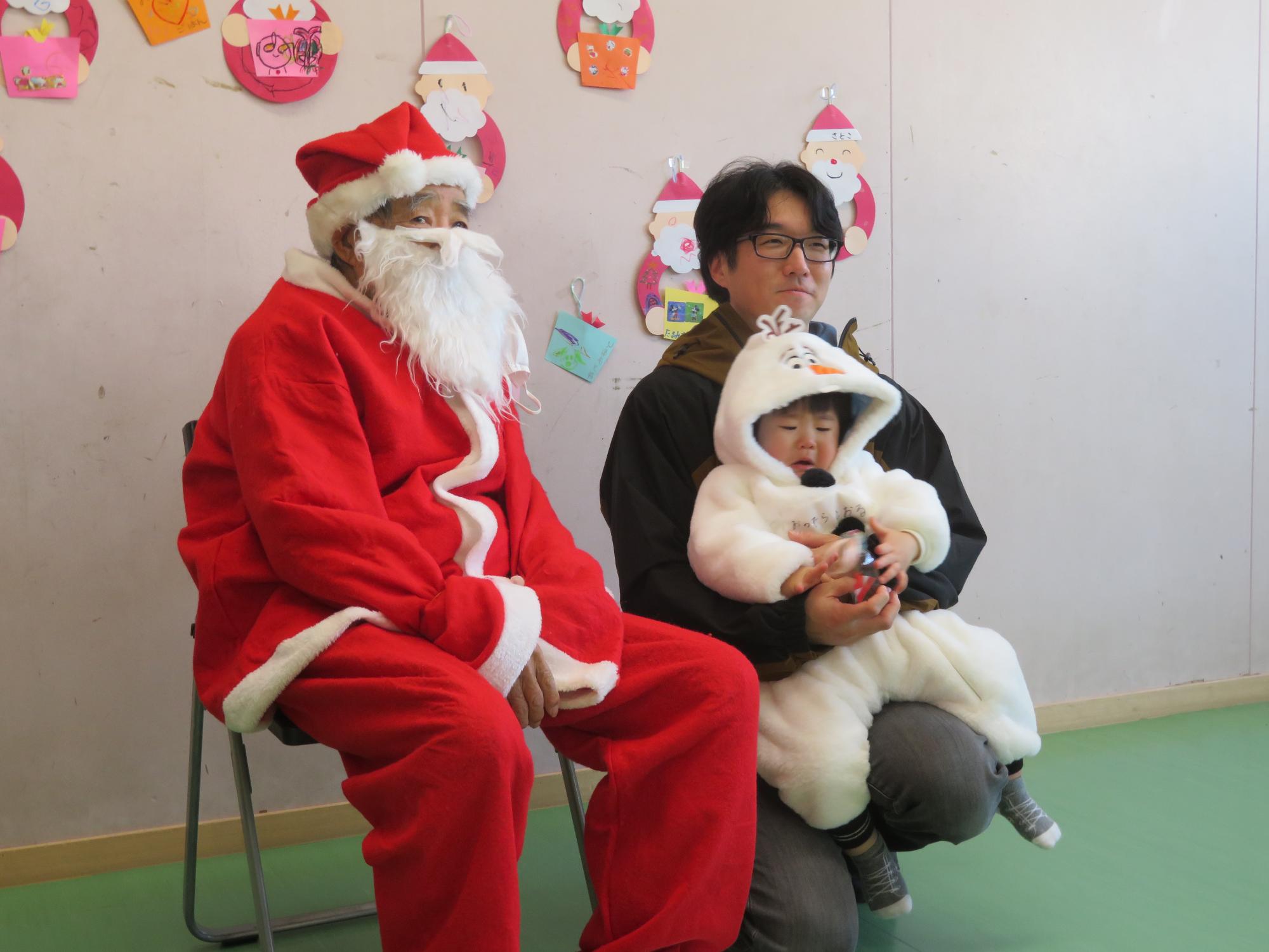 サンタに扮した地域ボランティアの方と写真を撮る幼児親子の写真