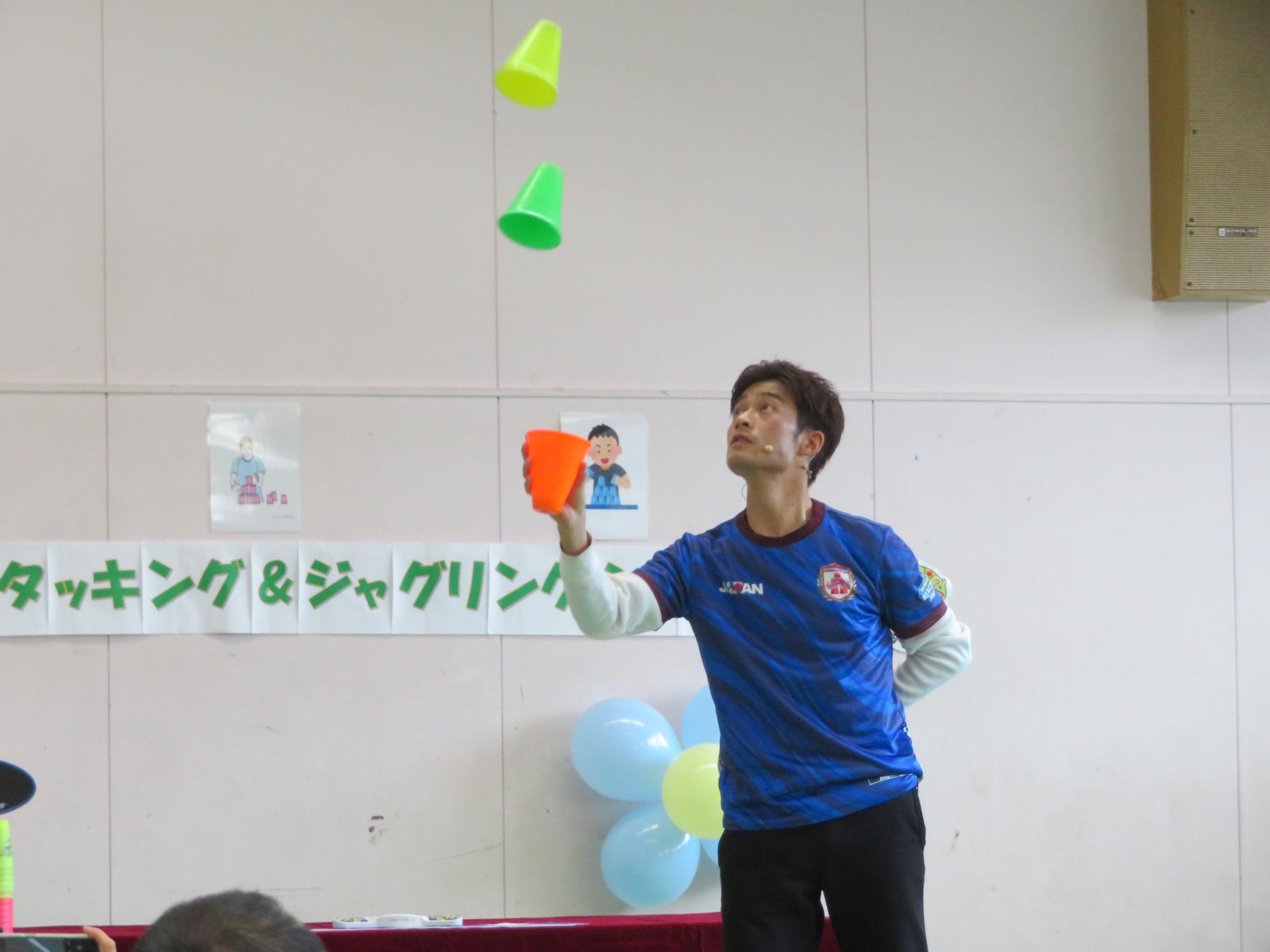 カップを使ったジャグリングを披露している講師の様子の写真