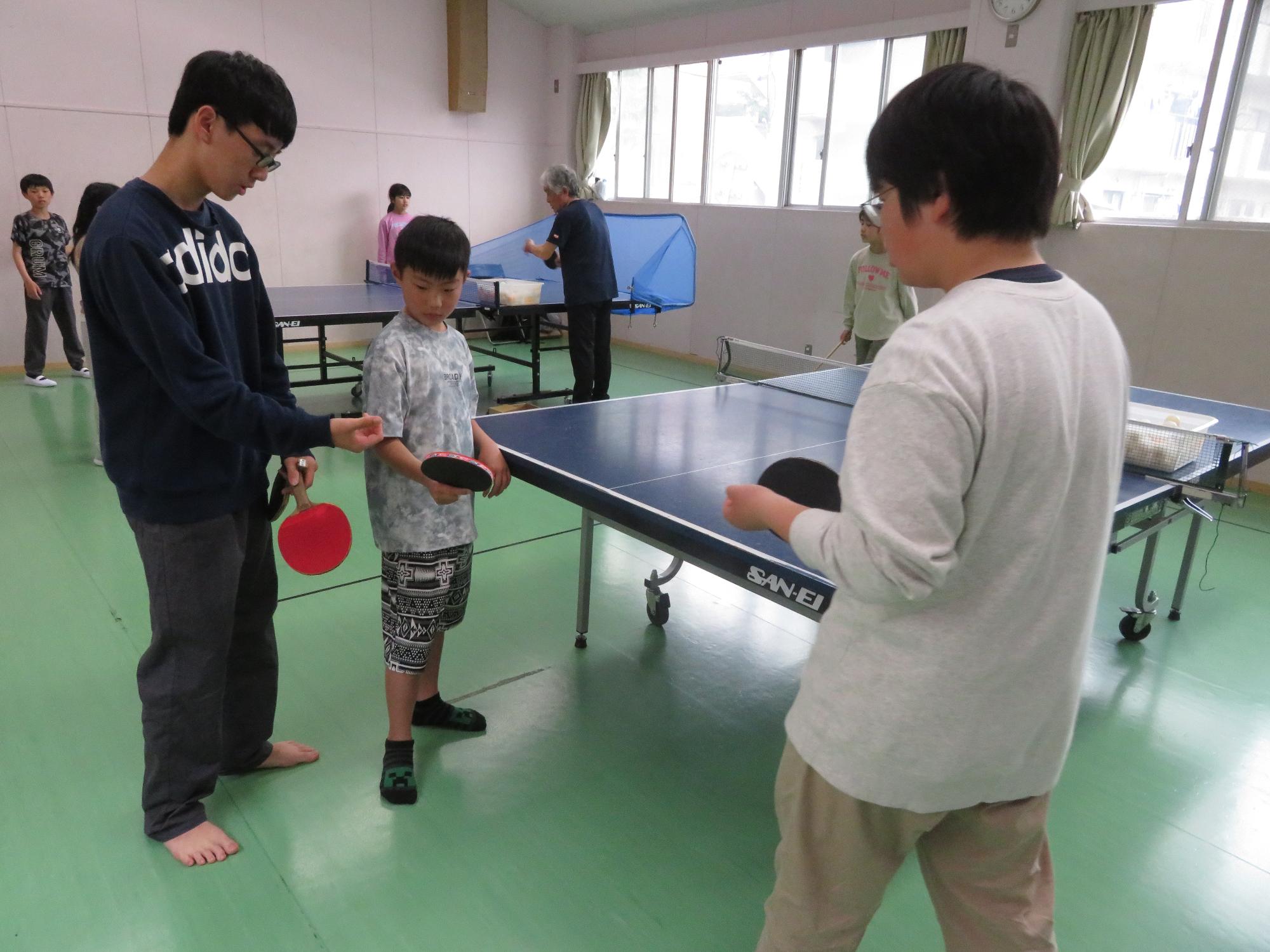 小学生に卓球の指導をする中学生の写真