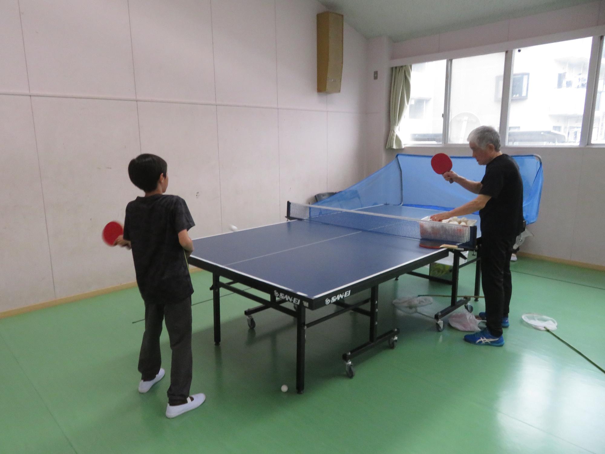 卓球の指導をするコーチと練習する児童
