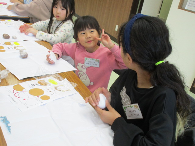 異年齢で粘土工作をし、女の子がカメラに向かってピースサインしている様子の写真