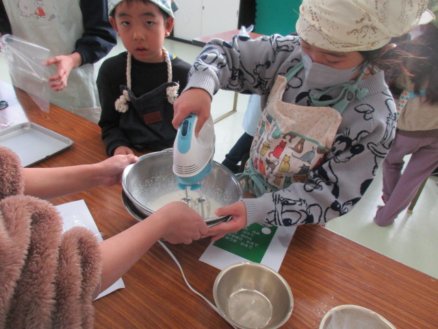 カップケーキにしぼるクリームをみんなで泡立てている写真