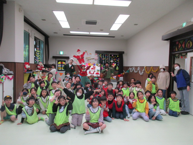 手作りのサンタクロースが壁に飾られ、カラフルな色のトナカイやツリーがガラス窓に貼られた室内でのスイートハンドのコンサート写真