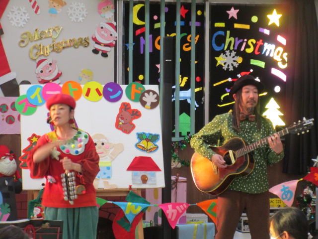 黒色の帽子を被った男性のギター演奏に合わせて、赤い服を着た女性ボーカルが両手の指を合わせて歌を歌っている「スイートハンド」さんの写真