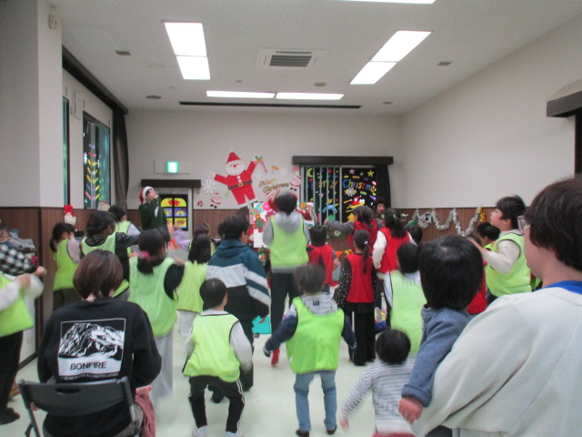 サンタの帽子を被った男性とスイートハンドのギターの演奏に合わせて子供たちが膝を曲げて歌っている様子の写真