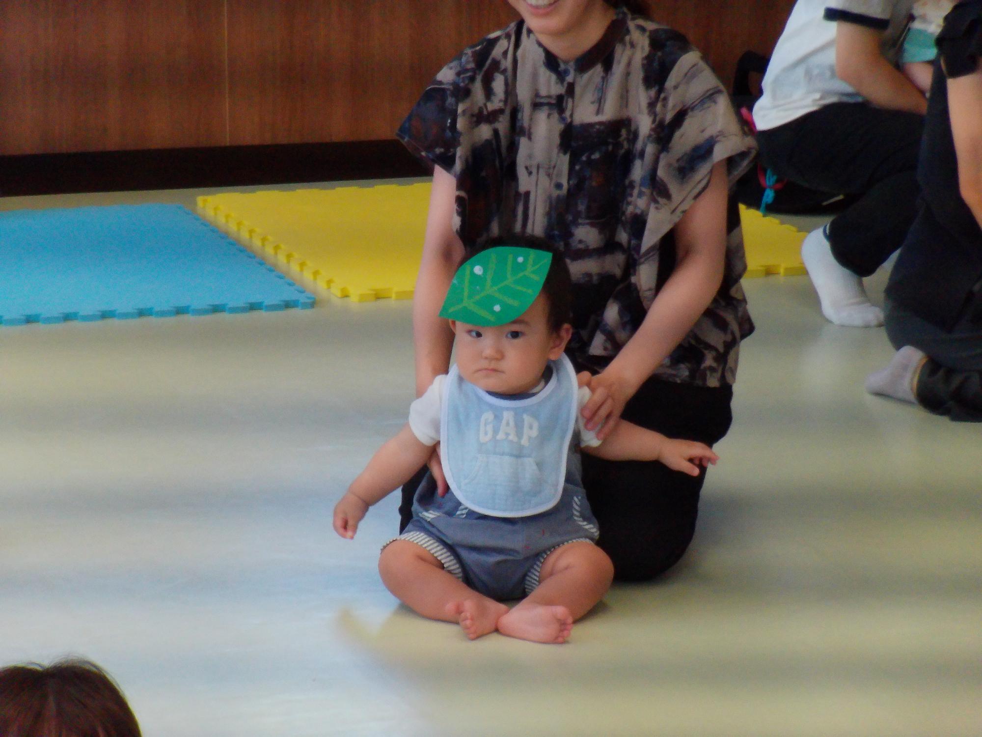 葉っぱのかざりを頭にのせた幼児の写真