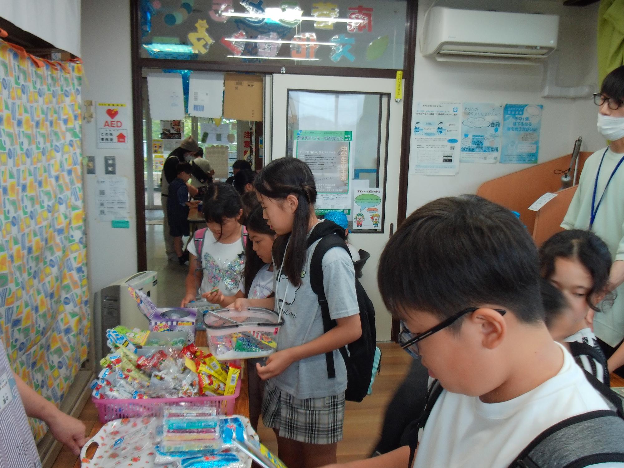 子供たちが駄菓子が並べられた机の周りでお菓子を選んでいる写真
