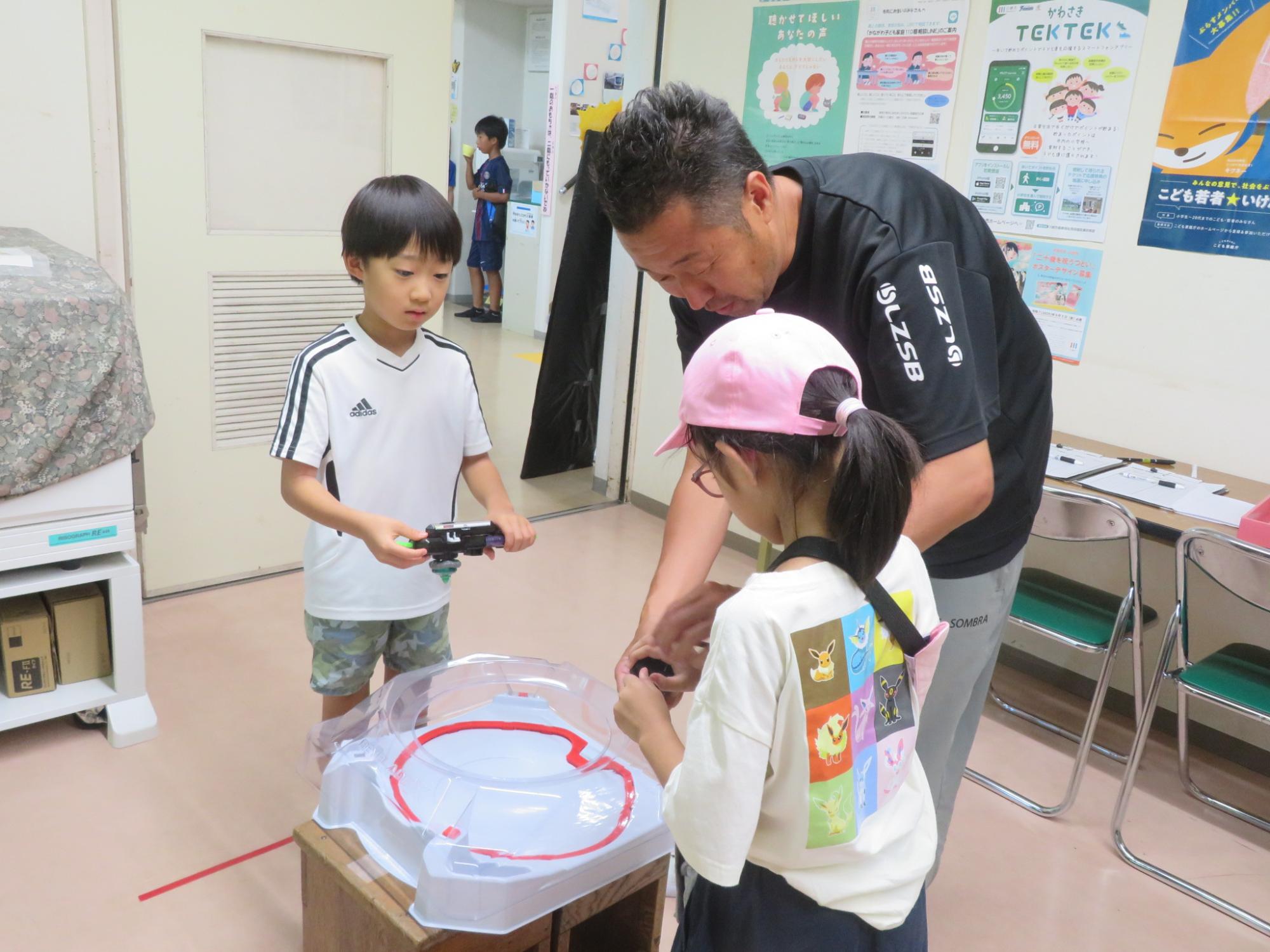 館長がこどもにベイブレードの回し方を教えている写真