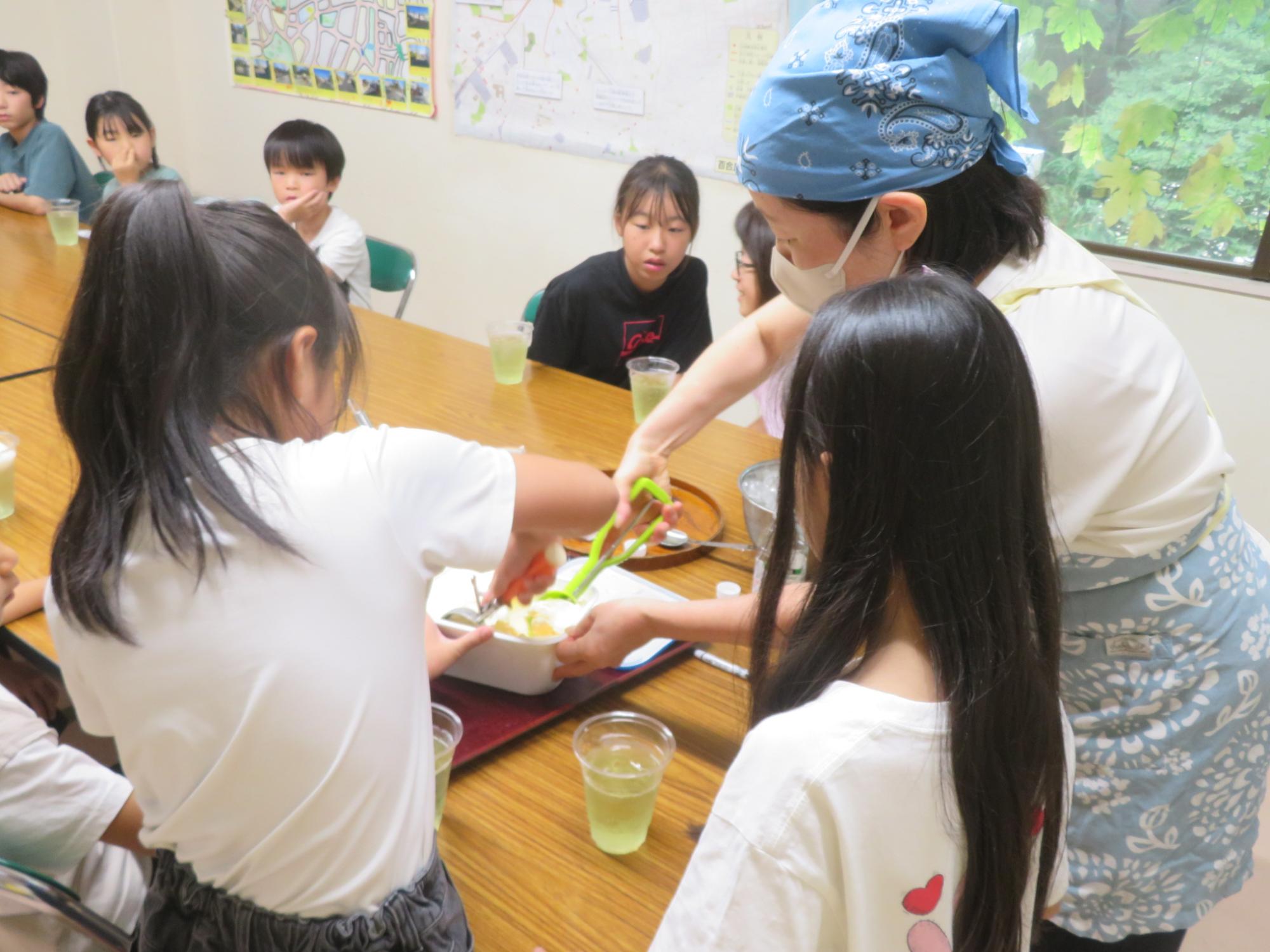 子どもとスタッフがアイスクリームをデッシャーですくっている写真