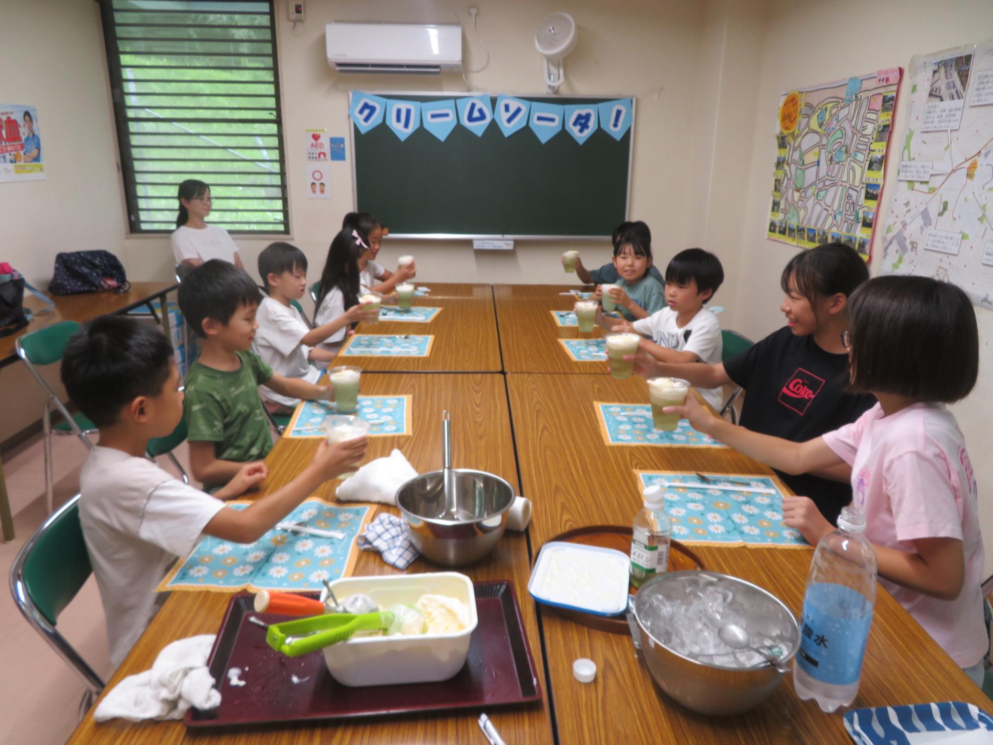 10名のこども達が自分で作ったクリームソーダを持って乾杯しようとしている写真