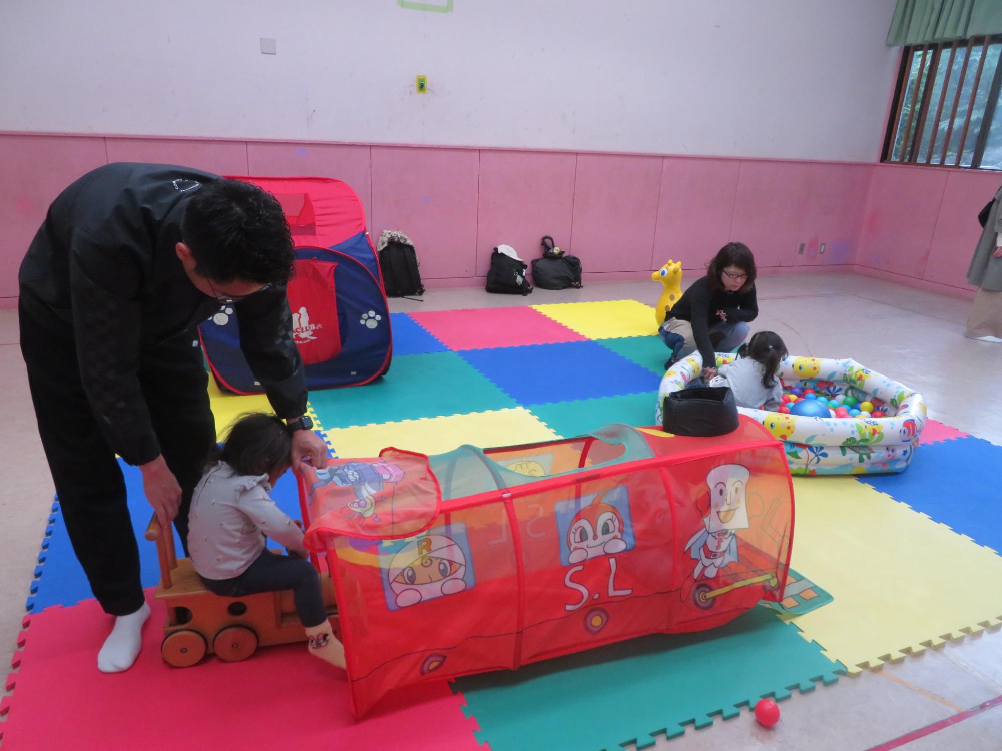 幼児が木の汽車の遊具に乗り、トンネルをくぐっている写真