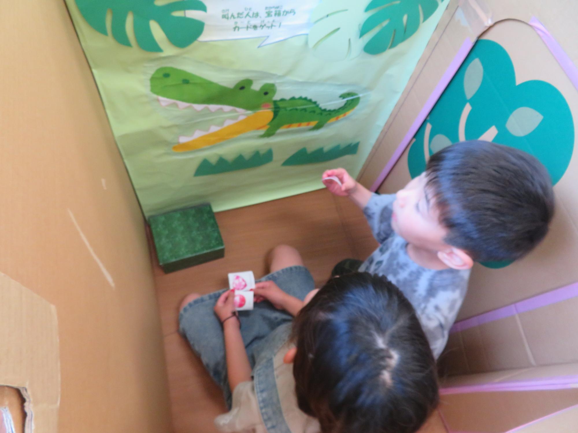 ダンボール迷路内のワニがだすミッションを読んでいる男の子の様子