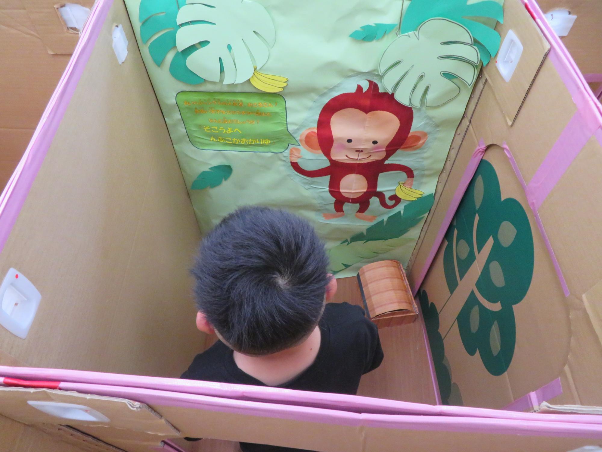 ダンボール迷路内の猿がだすミッションを読んでいる男の子の様子
