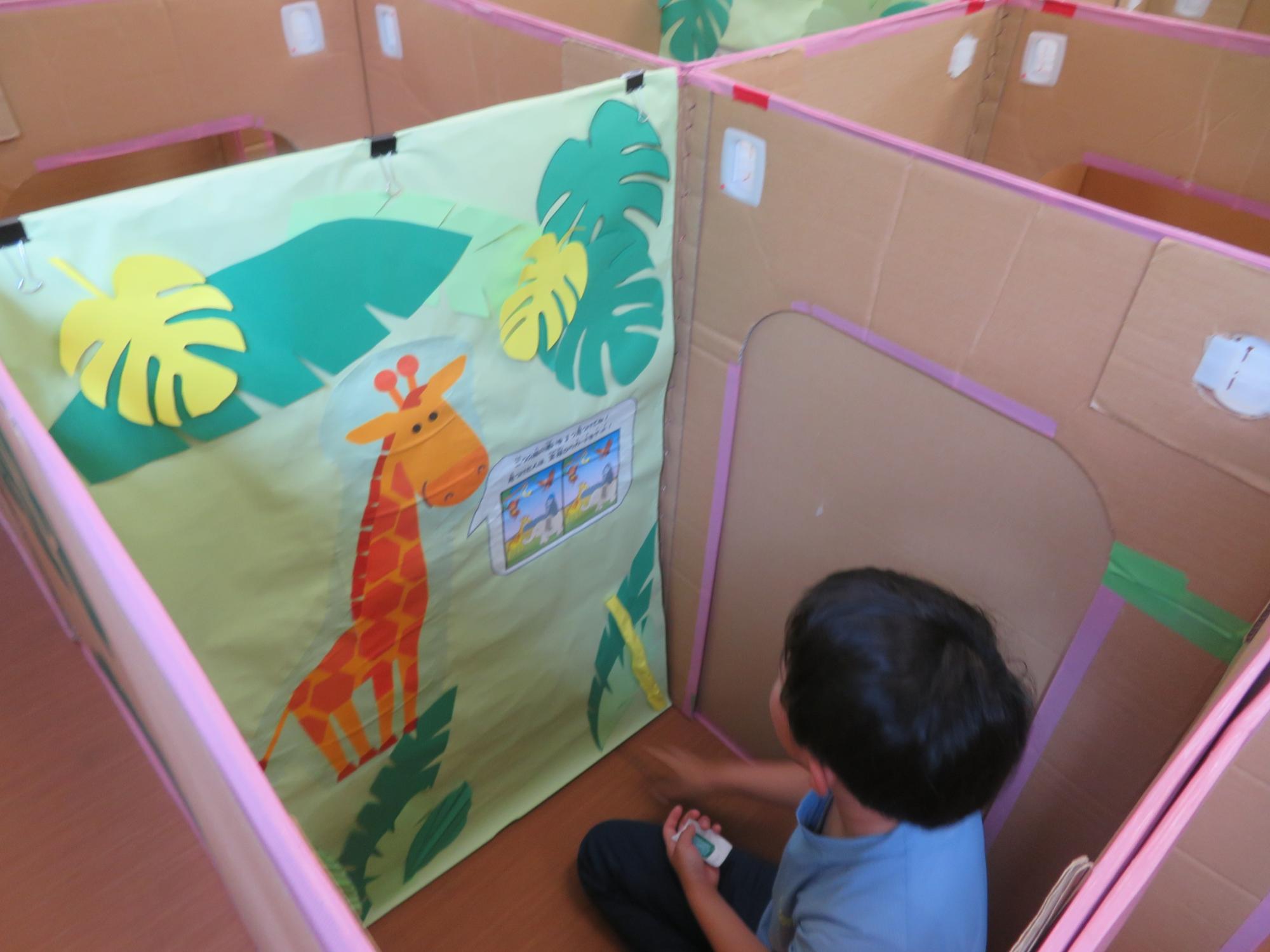 ダンボール迷路内のキリンがだす間違え探しのミッションを読んでいる男の子の様子