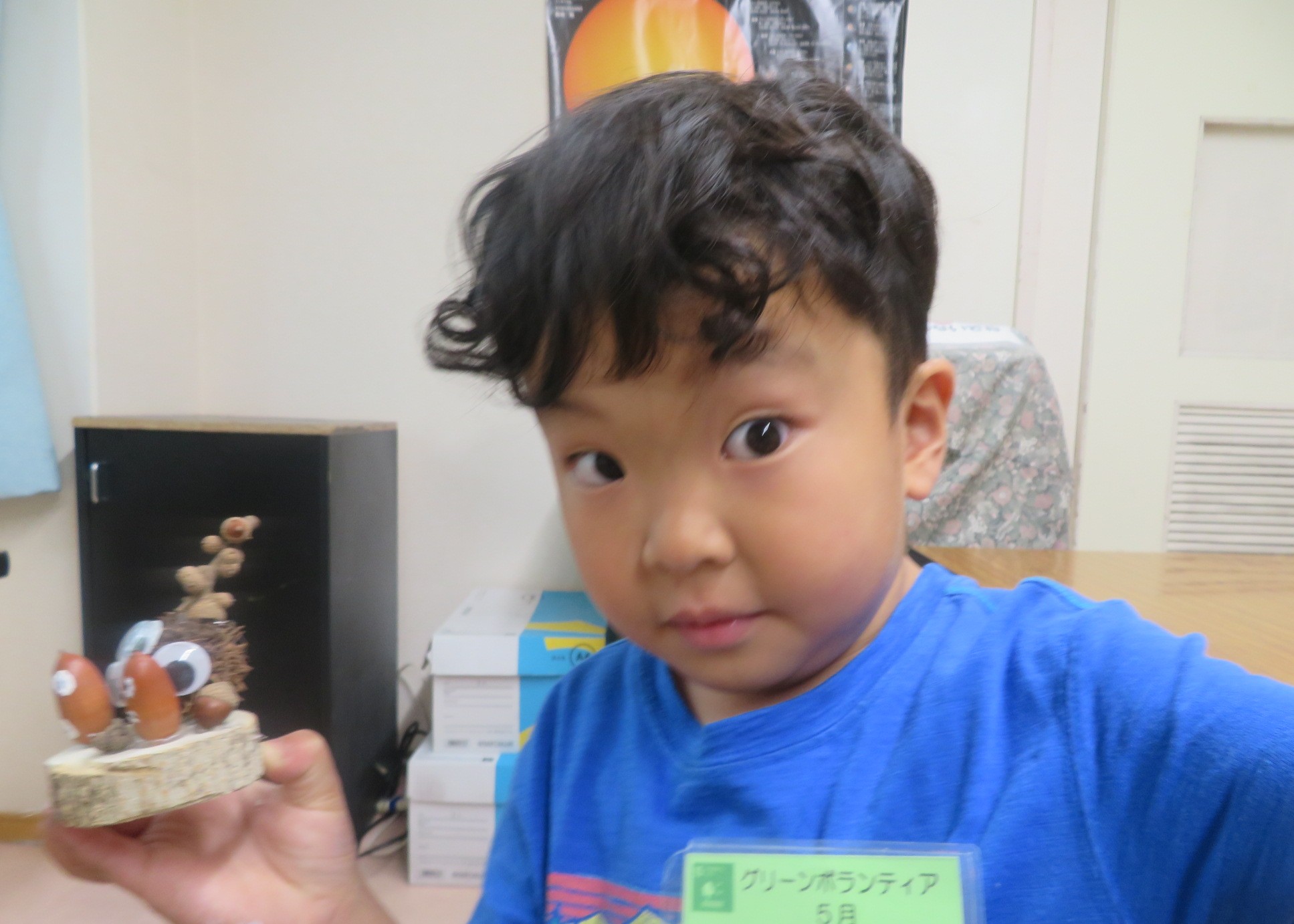 完成したどんぐり工作を持ってポーズしている幼児の男の子の様子