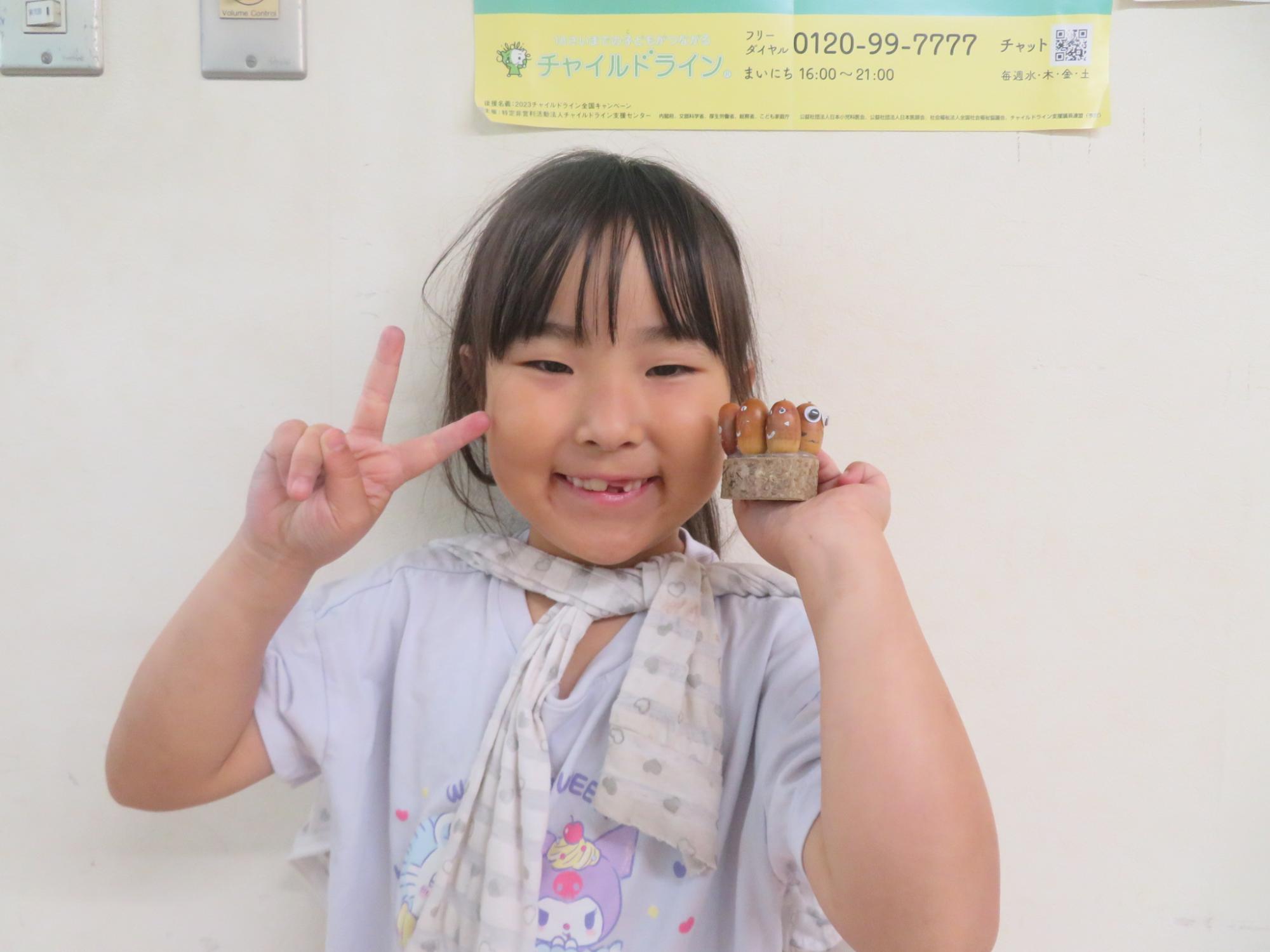 完成したどんぐり工作を持ってポーズしている小学生の女の子の様子