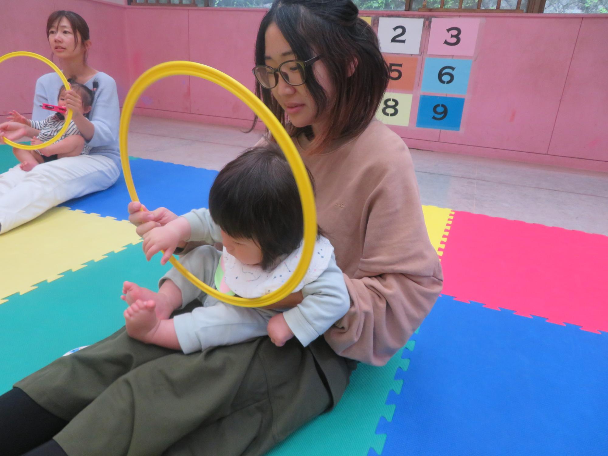 保護者の膝の上で、フープを使って遊ぶ幼児の様子