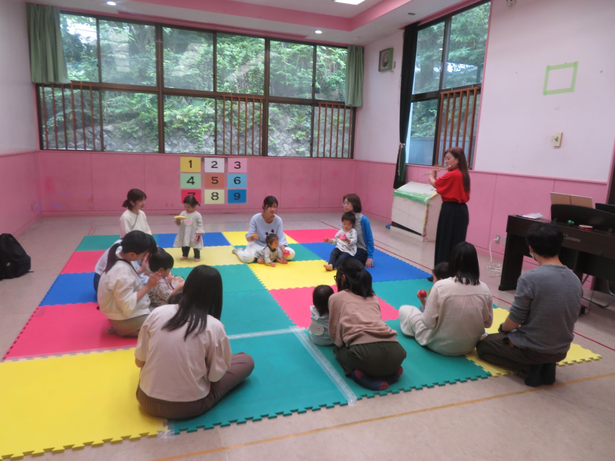 輪になって座り、講師のフルートの演奏を聴く親子の様子